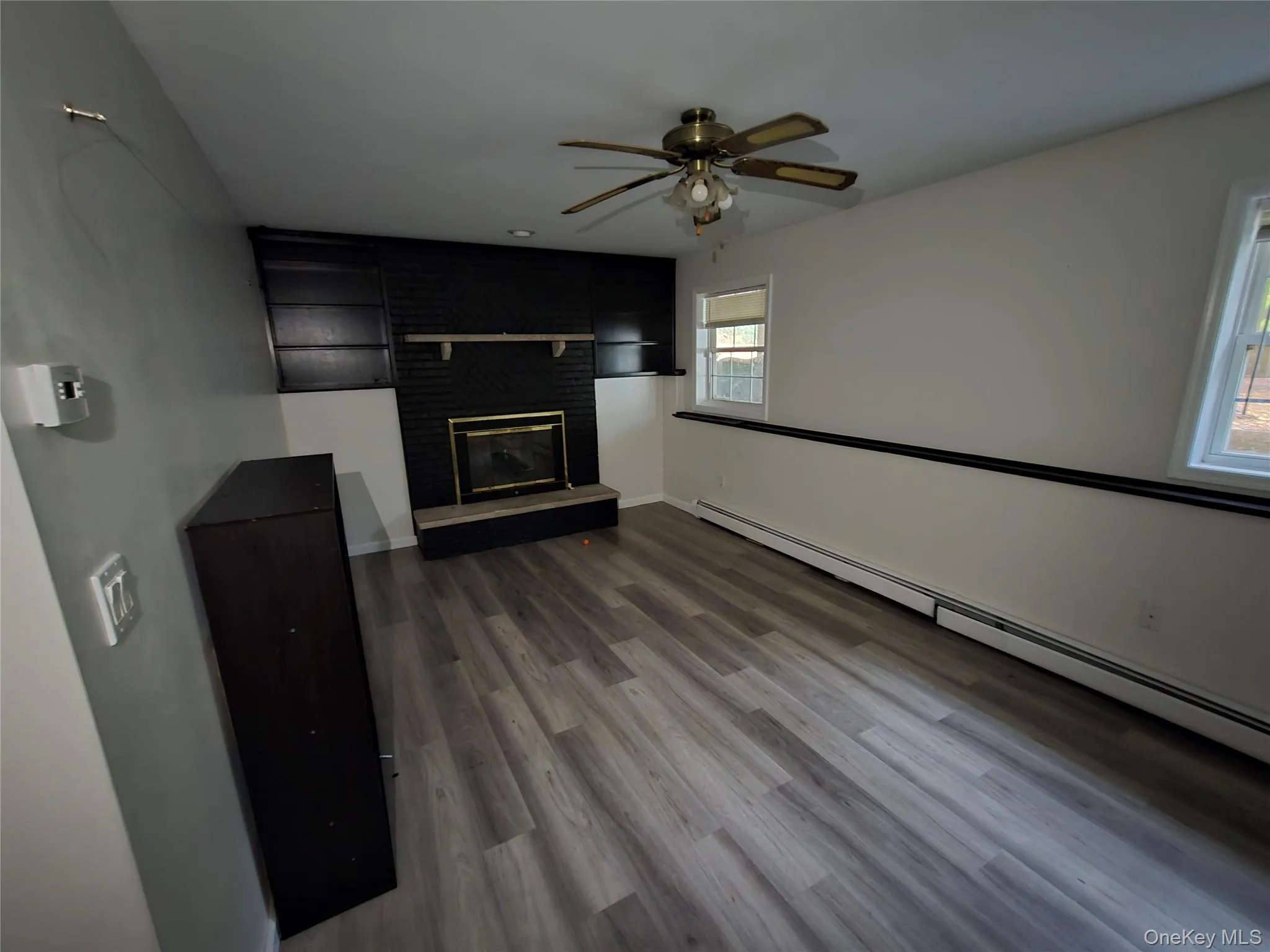 Unfurnished living room with a baseboard radiator, dark wood finished floors, a brick fireplace, and ceiling fan Unfurnished living room with a baseboard radiator, dark wood finished floors, a brick fireplace, and ceiling fan