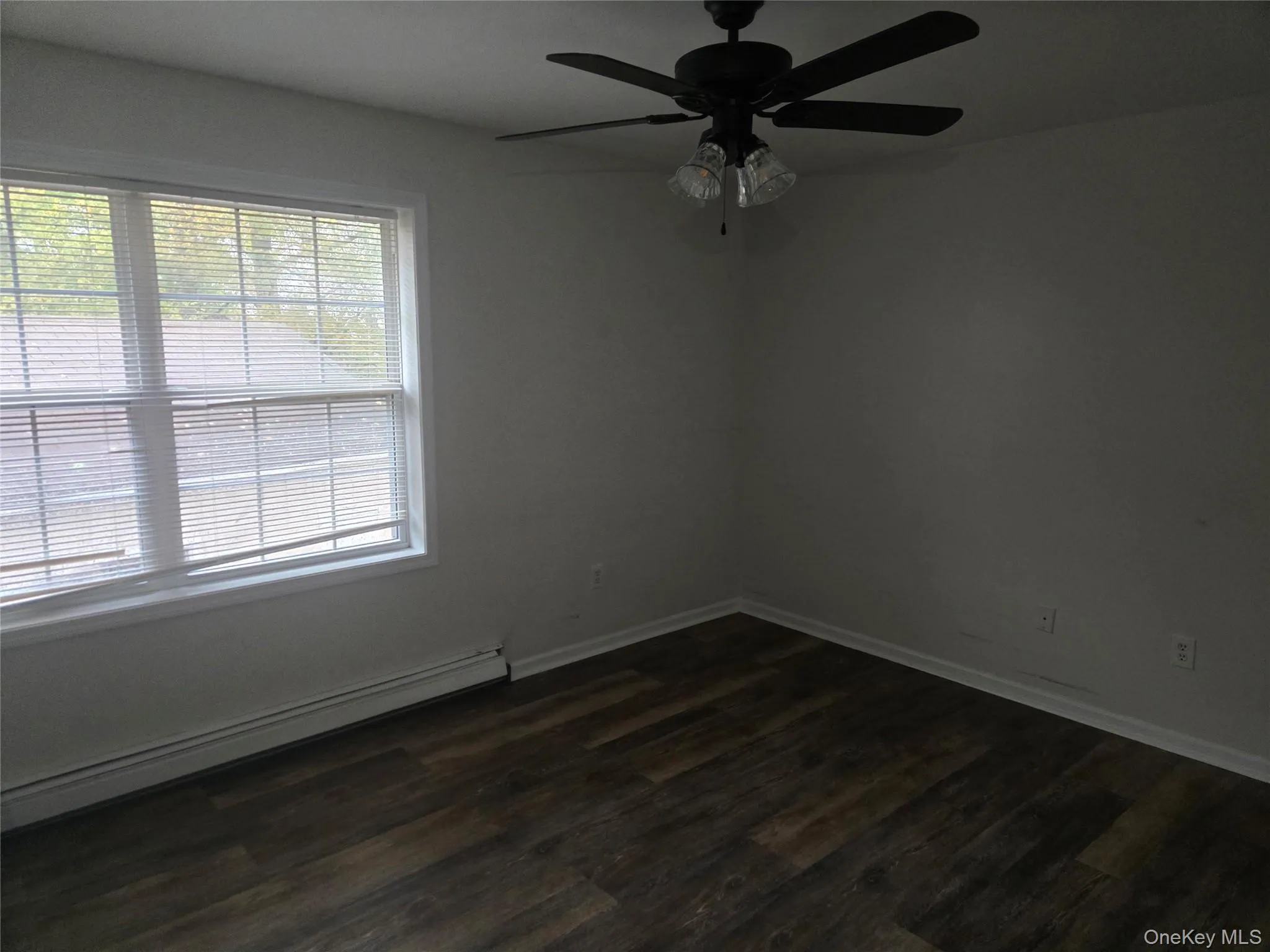 Empty room with baseboard heating, dark wood-type flooring, and ceiling fan Empty room with baseboard heating, dark wood-type flooring, and ceiling fan