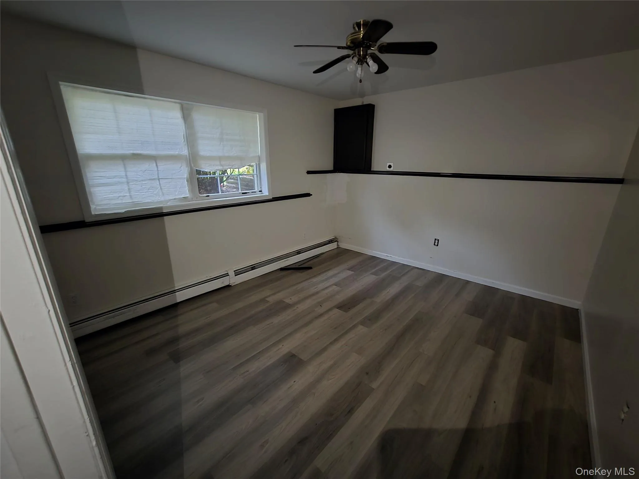 Spare room featuring wood finished floors, a baseboard heating unit, and a ceiling fan Spare room featuring wood finished floors, a baseboard heating unit, and a ceiling fan