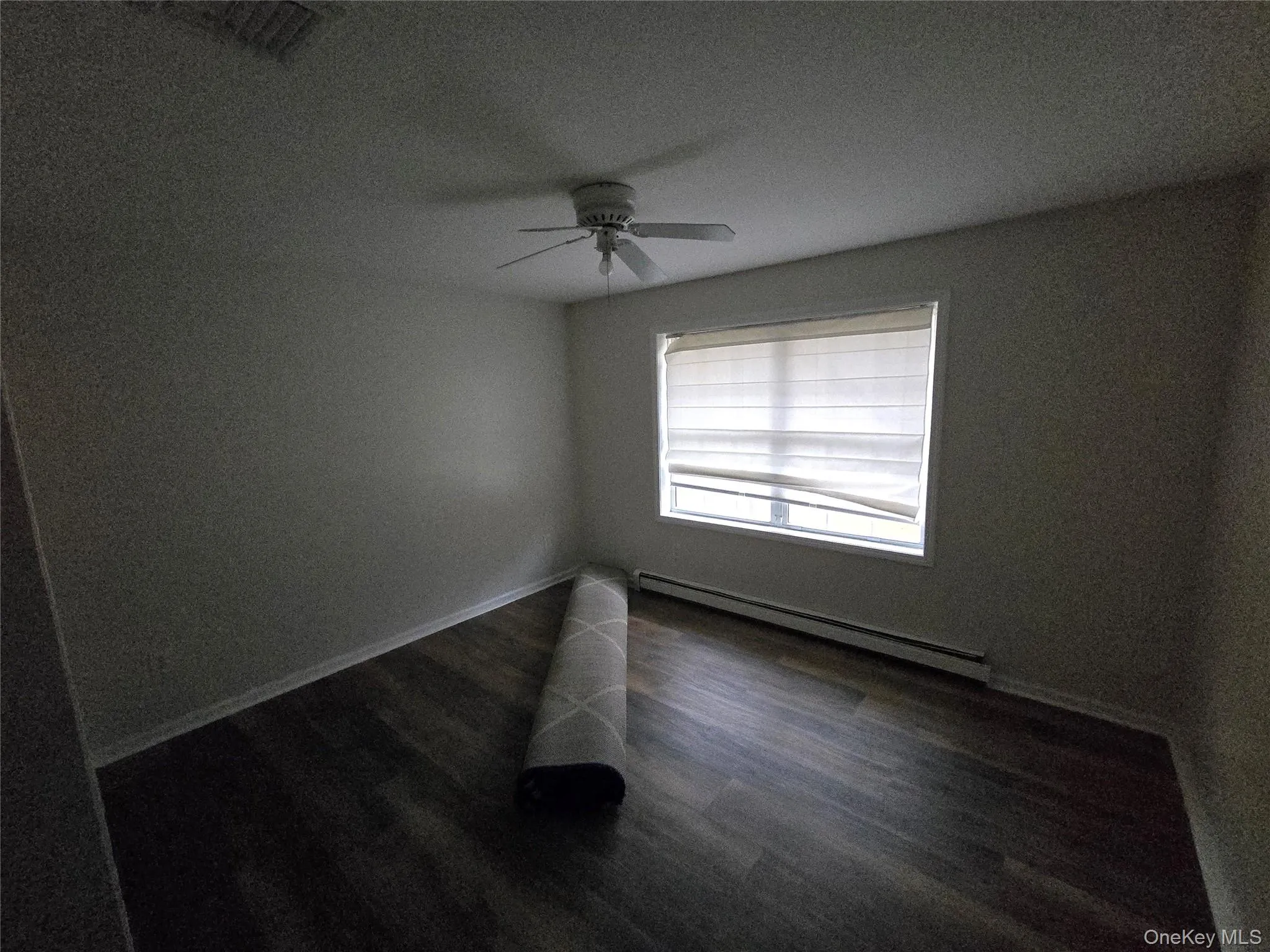Empty room featuring dark wood finished floors, baseboard heating, ceiling fan, and a textured ceiling Empty room featuring dark wood finished floors, baseboard heating, ceiling fan, and a textured ceiling
