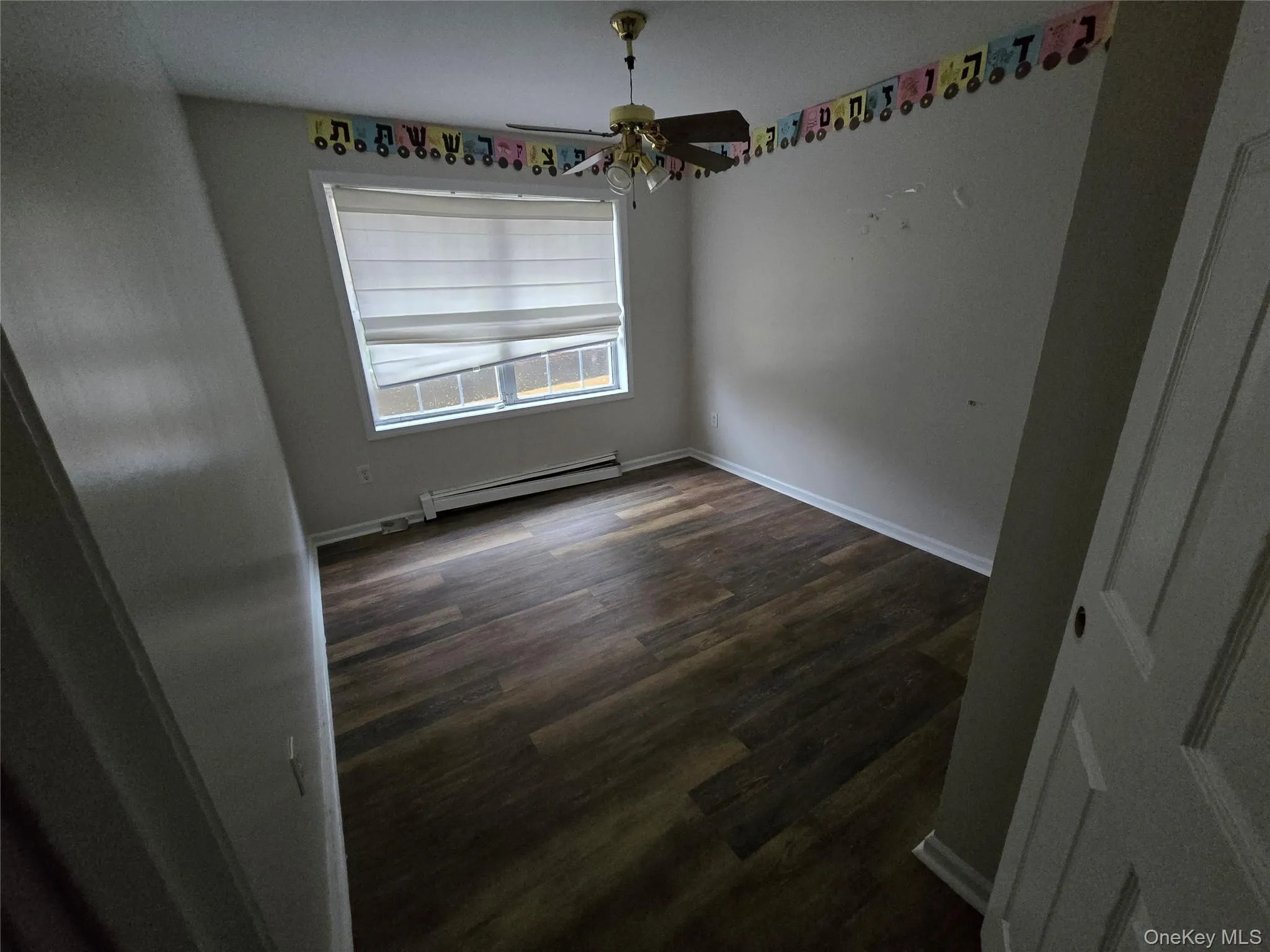 Empty room with a baseboard radiator, dark wood-type flooring, and a ceiling fan Empty room with a baseboard radiator, dark wood-type flooring, and a ceiling fan