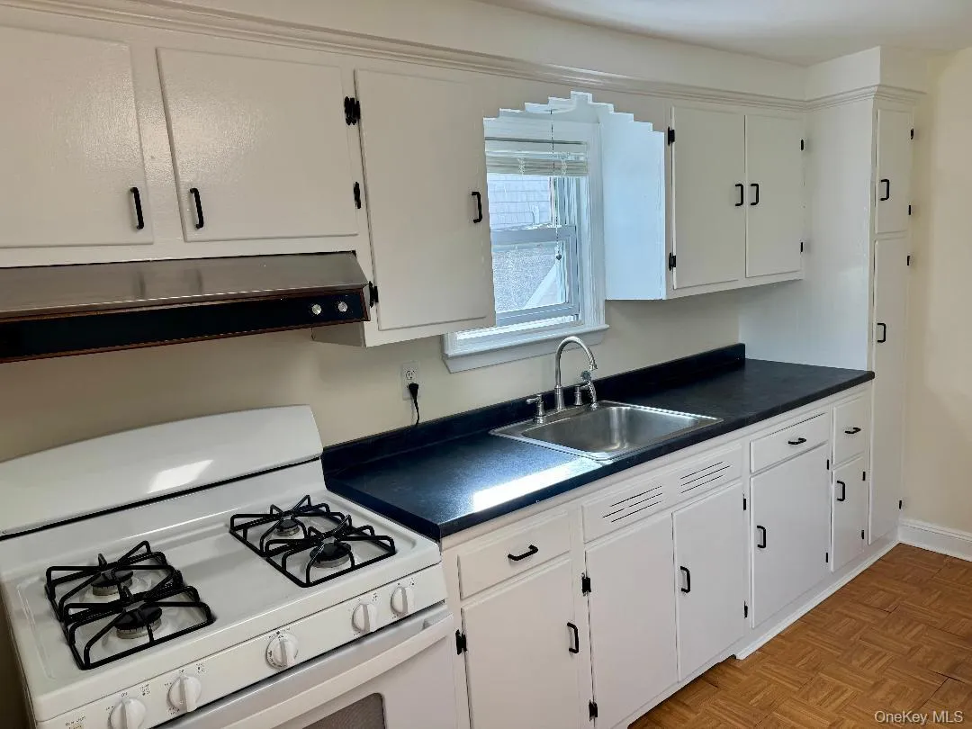 Kitchen with dark countertops, white range with gas cooktop, and white cabinets Kitchen with dark countertops, white range with gas cooktop, and white cabinets