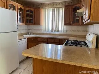 Kitchen featuring glass insert cabinets, brown cabinetry, white appliances, and light countertops Kitchen featuring glass insert cabinets, brown cabinetry, white appliances, and light countertops