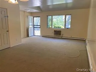Empty room with carpet flooring, a baseboard radiator, a baseboard heating unit, and an AC wall unit Empty room with carpet flooring, a baseboard radiator, a baseboard heating unit, and an AC wall unit