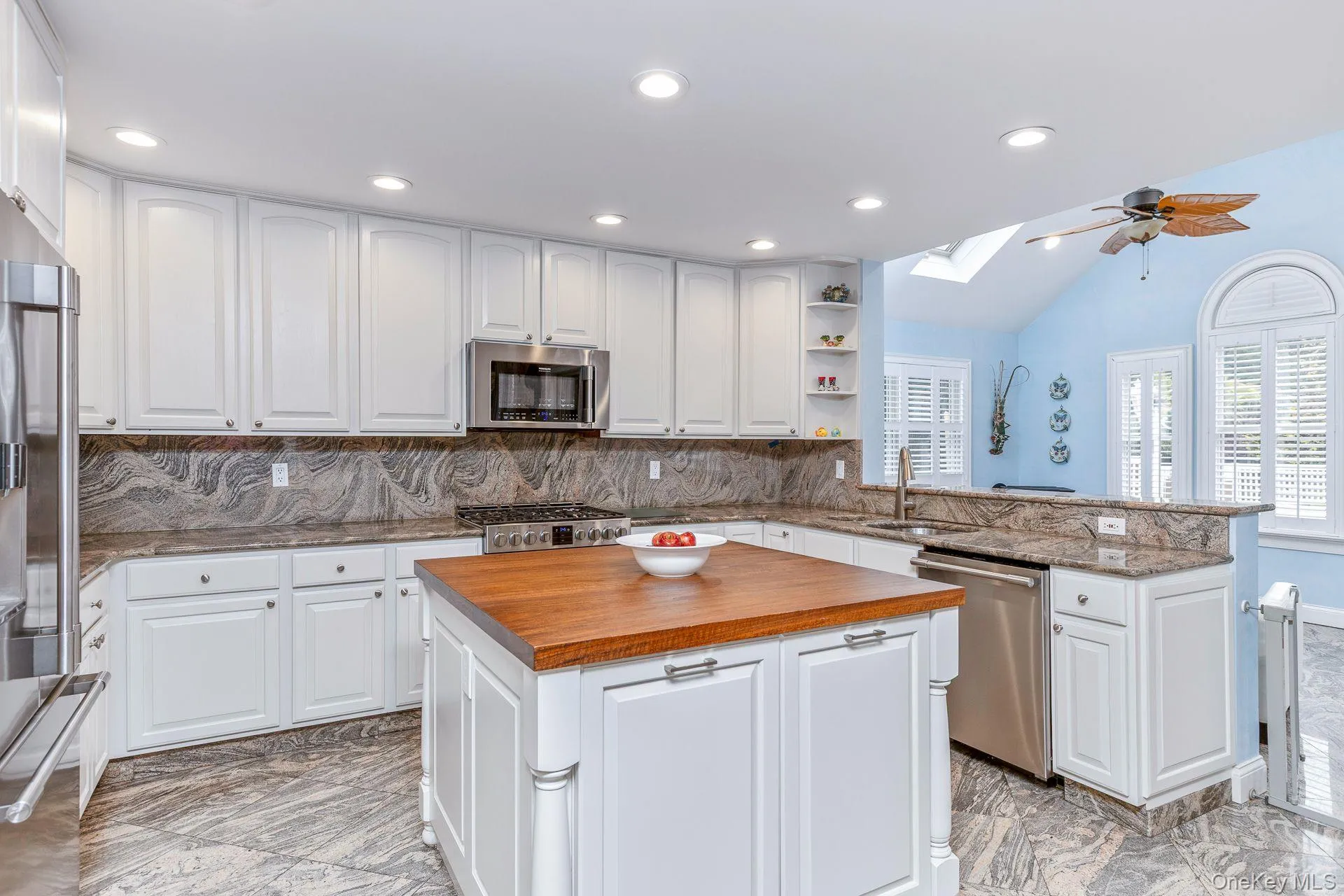 Kitchen featuring a skylight, decorative backsplash,granite countertops, white cabinetry, and vaulted ceiling Kitchen featuring a skylight, decorative backsplash,granite countertops, white cabinetry, and vaulted ceiling