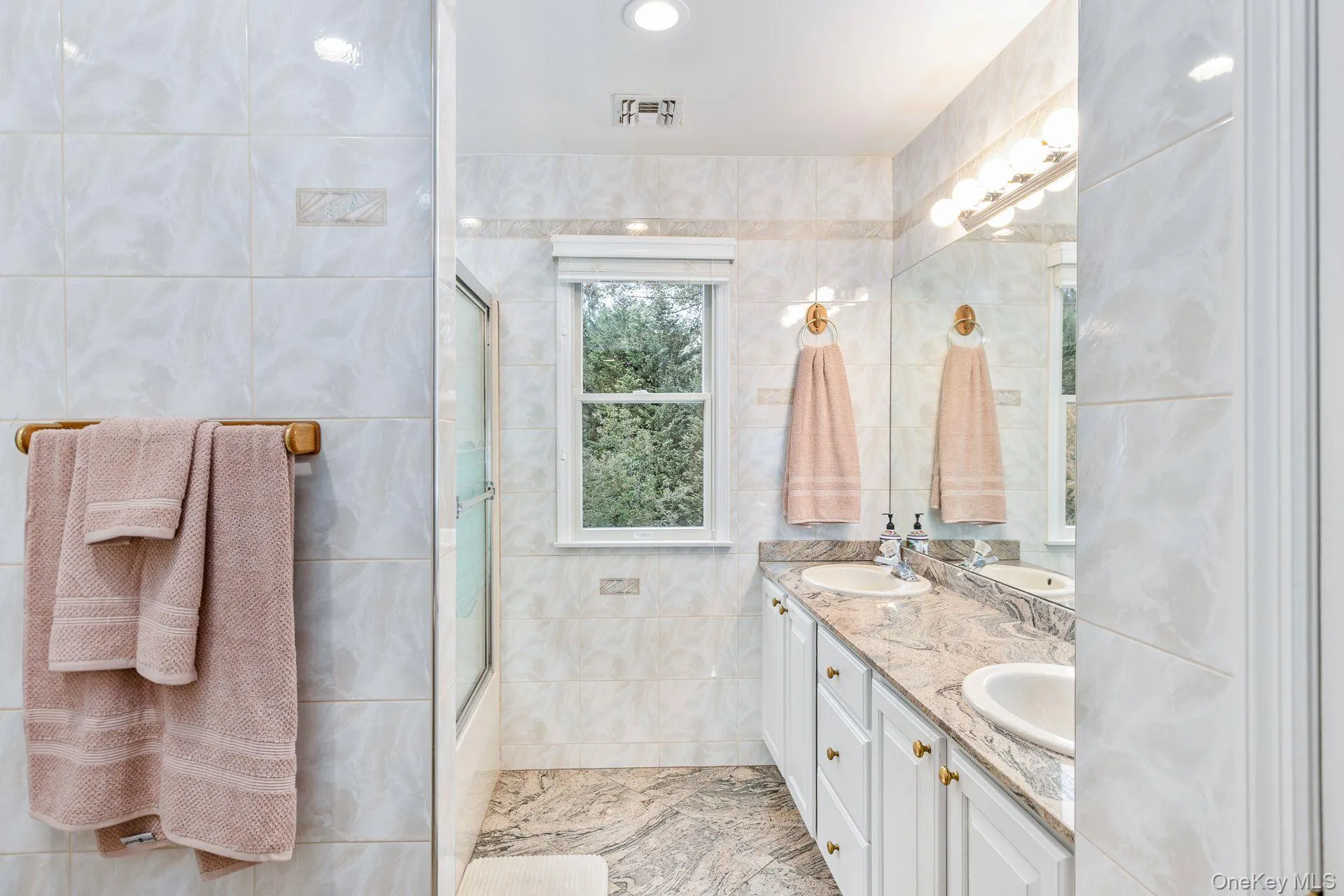 Bathroom featuring tile walls, double vanity, bath / shower combo with glass door, and recessed lighting Bathroom featuring tile walls, double vanity, bath / shower combo with glass door, and recessed lighting