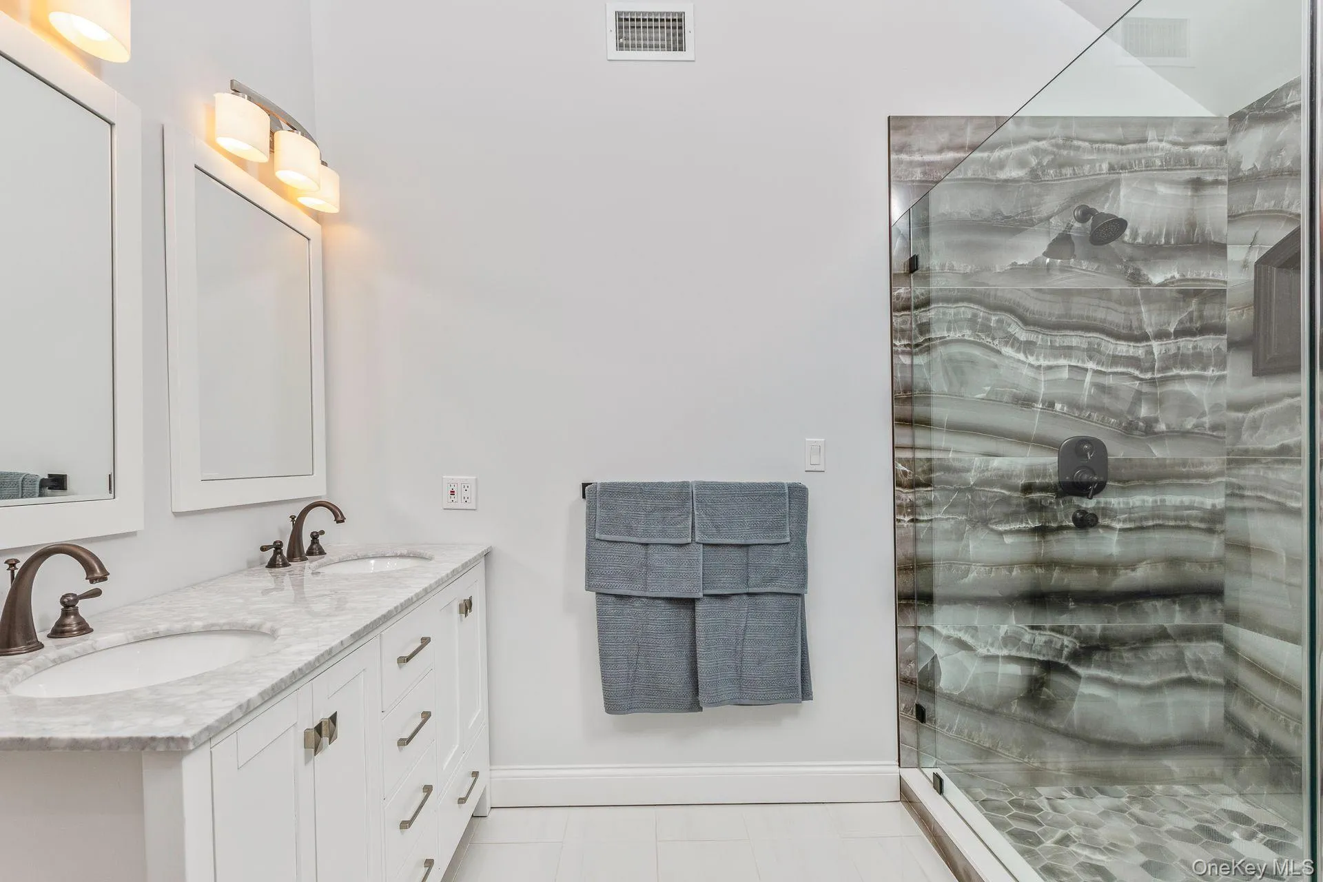 Bathroom featuring double vanity, a marble finish shower, and light tile patterned flooring Bathroom featuring double vanity, a marble finish shower, and light tile patterned flooring