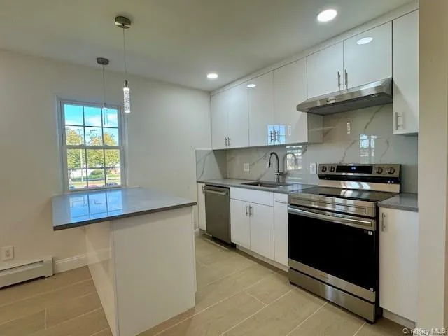 Kitchen featuring stainless steel appliances, white cabinetry, under cabinet range hood, pendant lighting, and backsplash Kitchen featuring stainless steel appliances, white cabinetry, under cabinet range hood, pendant lighting, and backsplash