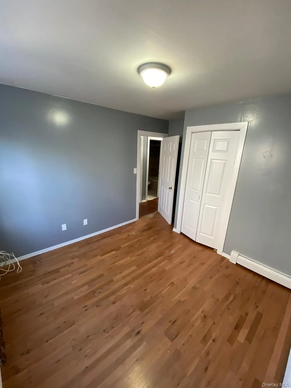 Unfurnished bedroom featuring dark wood finished floors, a closet, and a baseboard radiator Unfurnished bedroom featuring dark wood finished floors, a closet, and a baseboard radiator