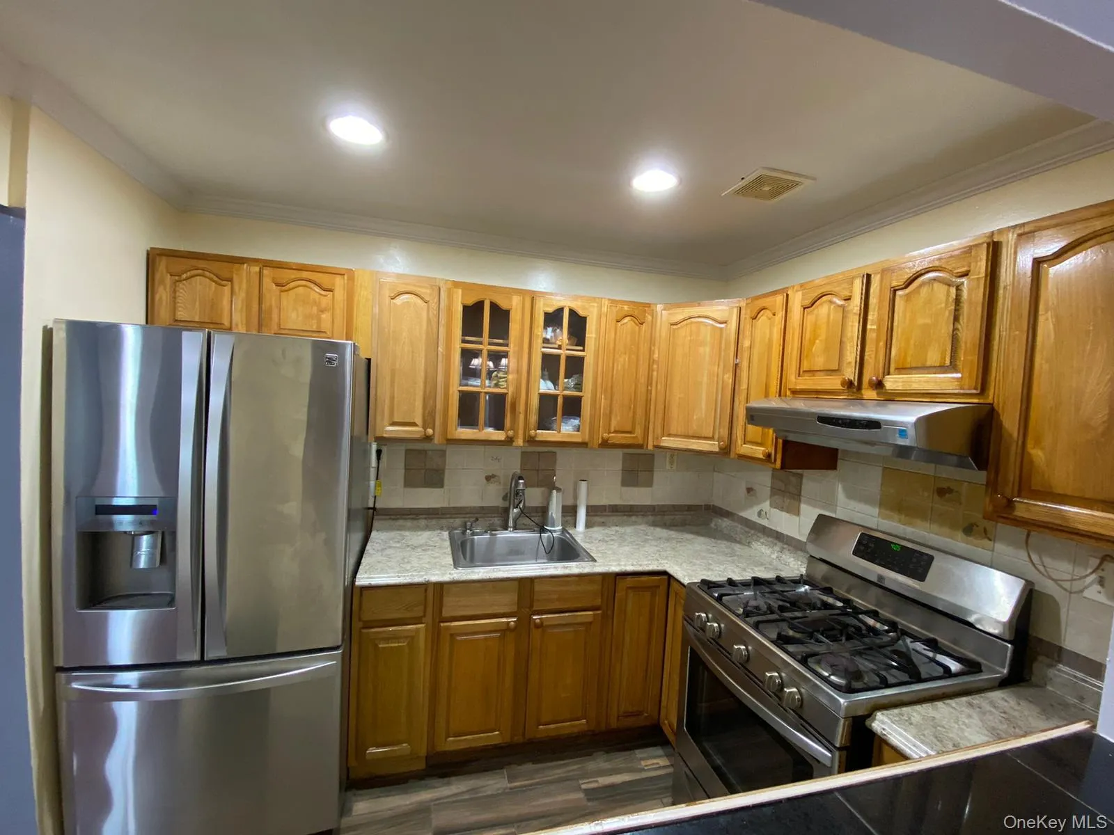 Kitchen with appliances with stainless steel finishes, tasteful backsplash, glass insert cabinets, light countertops, and crown molding Kitchen with appliances with stainless steel finishes, tasteful backsplash, glass insert cabinets, light countertops, and crown molding