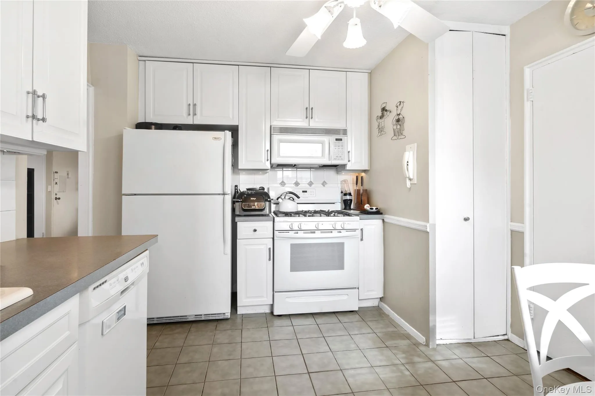 Kitchen with white cabinets, white appliances, and light tile patterned floors Kitchen with white cabinets, white appliances, and light tile patterned floors