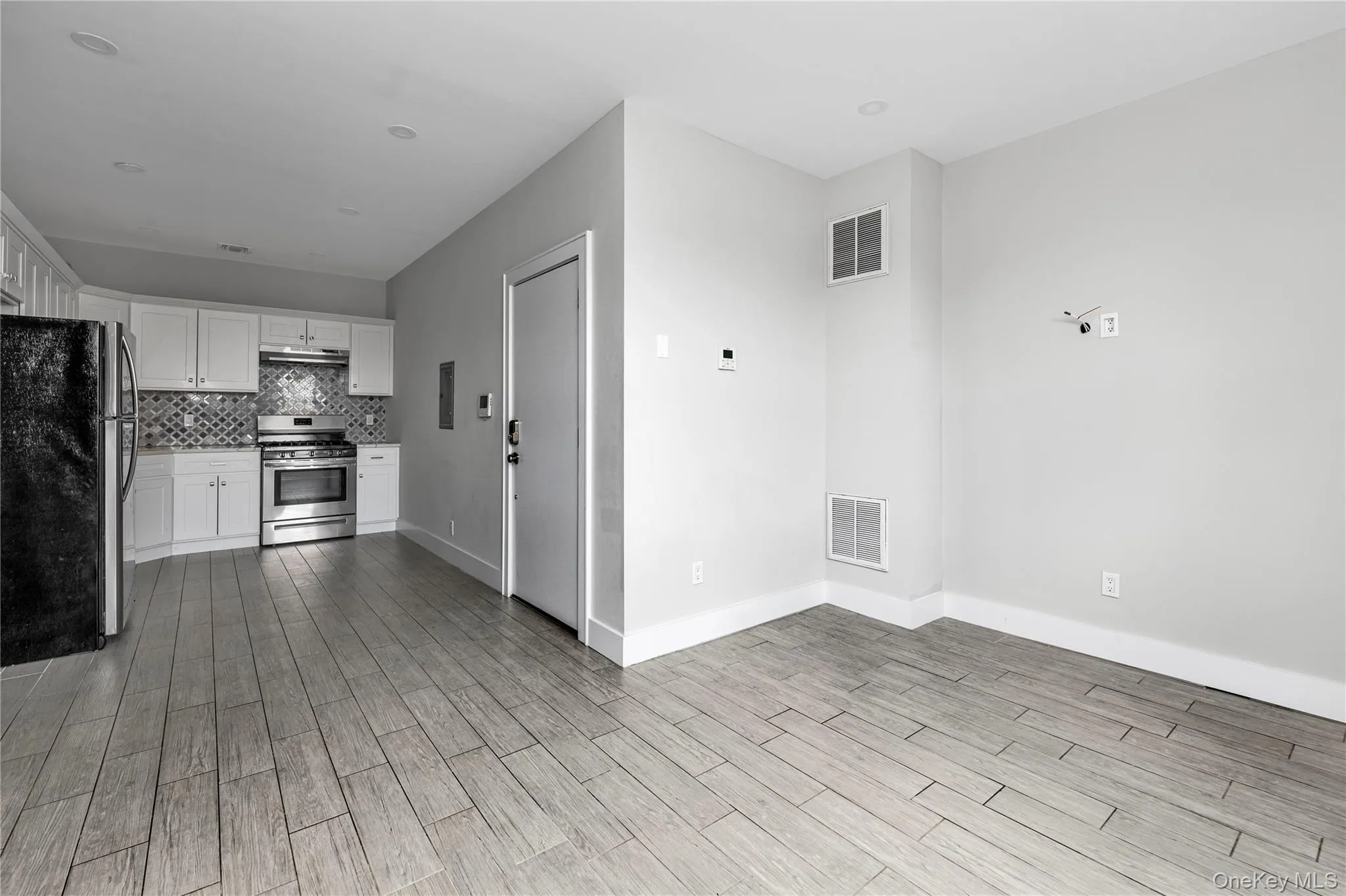 Kitchen with stainless steel appliances, white cabinets, decorative backsplash, light wood-style flooring, and under cabinet range hood Kitchen with stainless steel appliances, white cabinets, decorative backsplash, light wood-style flooring, and under cabinet range hood