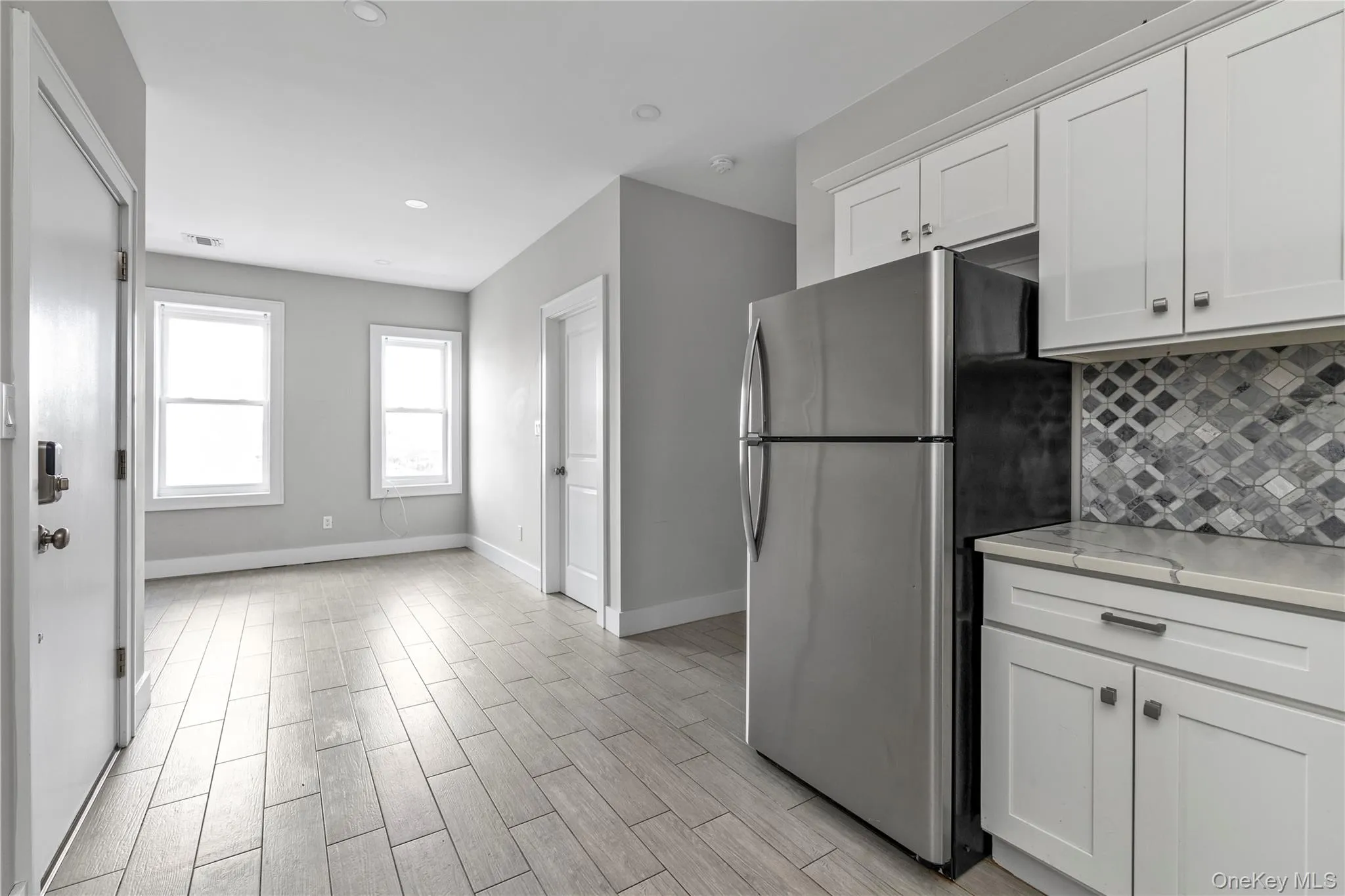 Kitchen featuring freestanding refrigerator, white cabinetry, wood finish floors, backsplash, and recessed lighting Kitchen featuring freestanding refrigerator, white cabinetry, wood finish floors, backsplash, and recessed lighting