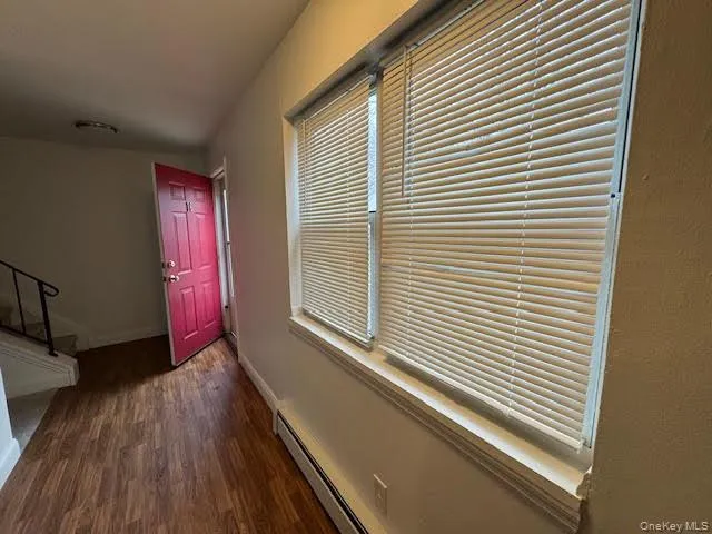Hallway featuring a baseboard heating unit, dark wood-style flooring, and stairway Hallway featuring a baseboard heating unit, dark wood-style flooring, and stairway