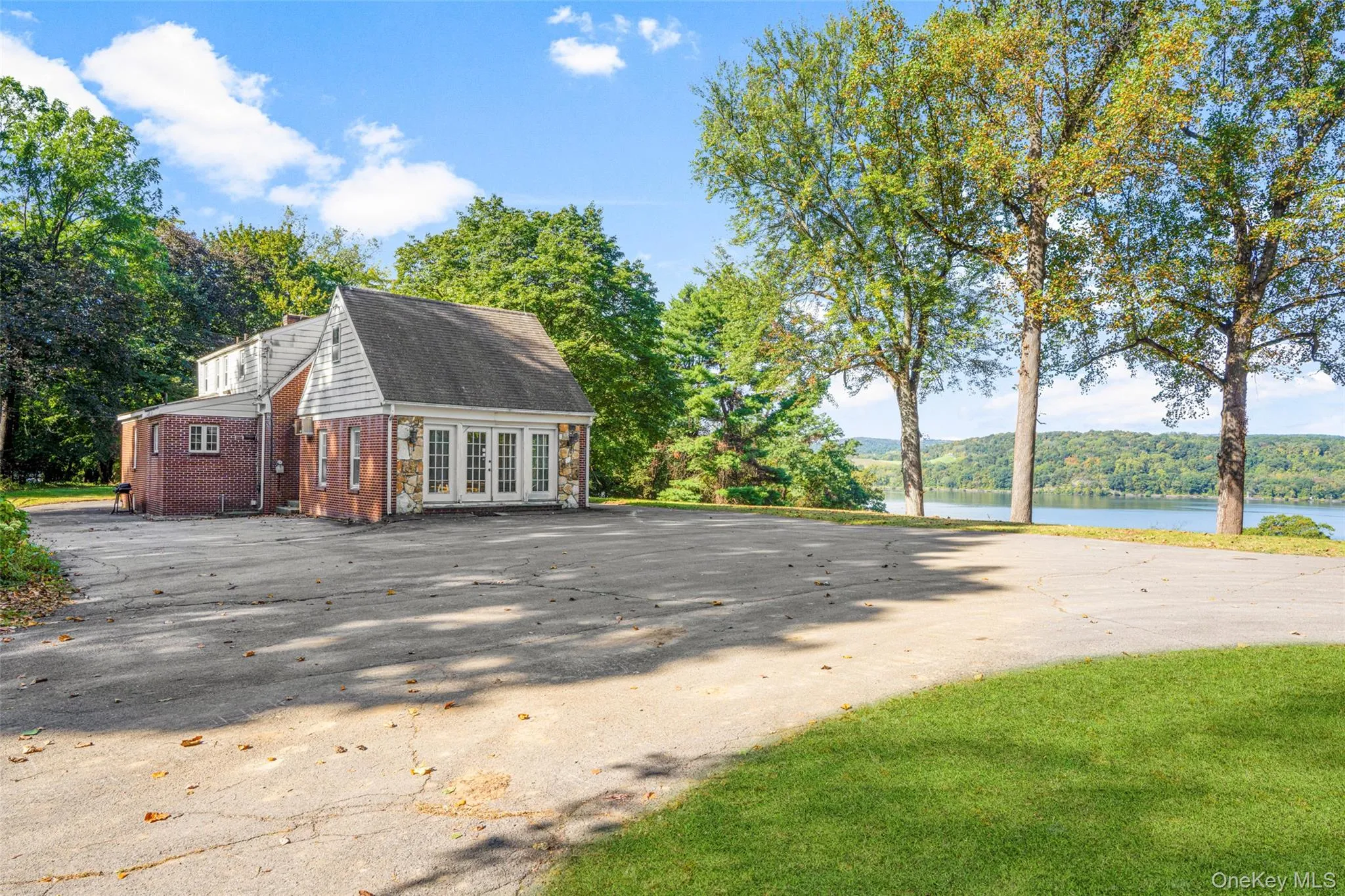 View of property exterior with brick siding, french doors, a water view, driveway, and a view of trees View of property exterior with brick siding, french doors, a water view, driveway, and a view of trees