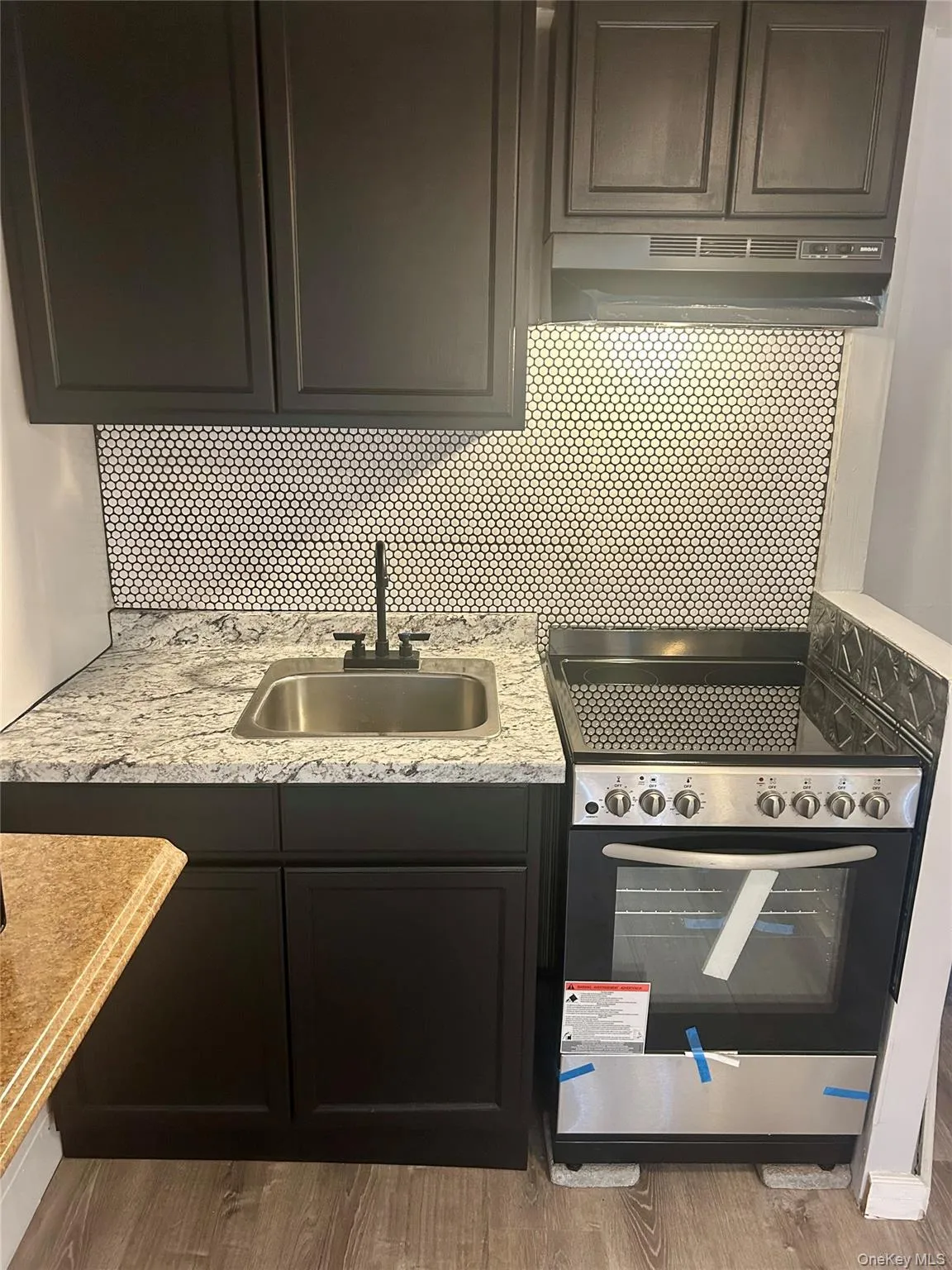 Kitchen with stainless steel range with electric cooktop, under cabinet range hood, light stone countertops, decorative backsplash, and light wood finished floors Kitchen with stainless steel range with electric cooktop, under cabinet range hood, light stone countertops, decorative backsplash, and light wood finished floors