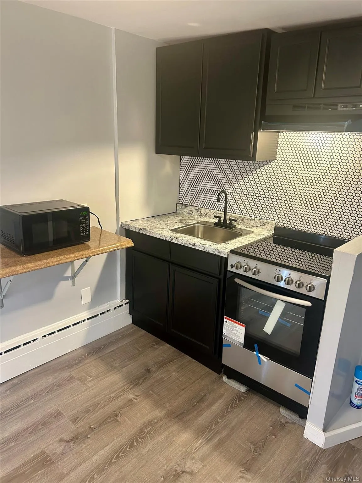 Kitchen featuring a baseboard heating unit, dark cabinets, black microwave, electric range, and backsplash Kitchen featuring a baseboard heating unit, dark cabinets, black microwave, electric range, and backsplash