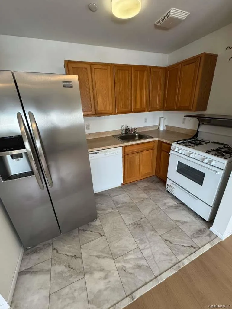 Kitchen featuring white appliances, brown cabinetry, and light countertops Kitchen featuring white appliances, brown cabinetry, and light countertops