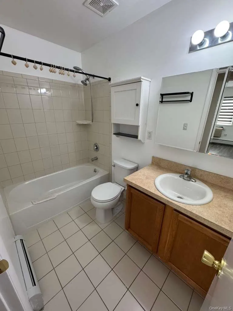 Bathroom featuring bathing tub / shower combination, vanity, baseboard heating, and light tile patterned floors Bathroom featuring bathing tub / shower combination, vanity, baseboard heating, and light tile patterned floors