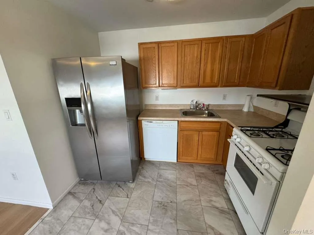 Kitchen with white appliances, light countertops, brown cabinets, and light marble finish flooring Kitchen with white appliances, light countertops, brown cabinets, and light marble finish flooring