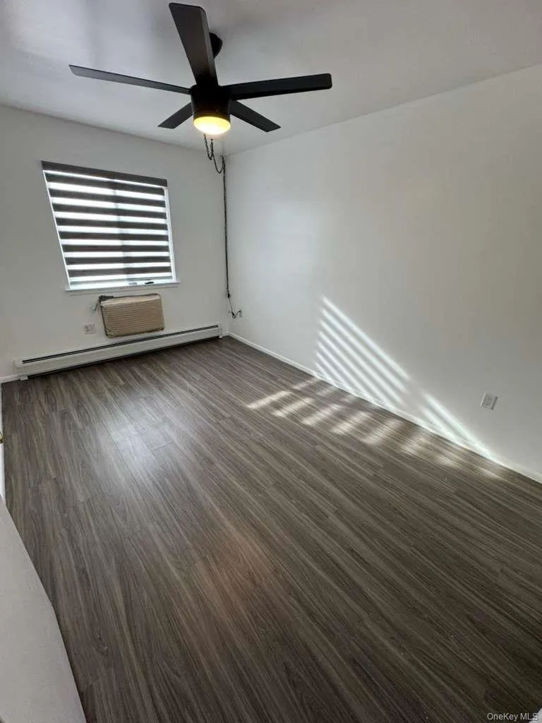 Spare room with a baseboard heating unit, dark wood-style flooring, and a ceiling fan Spare room with a baseboard heating unit, dark wood-style flooring, and a ceiling fan