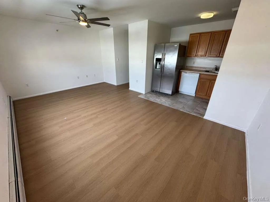 Kitchen with brown cabinetry, light wood-type flooring, ceiling fan, dishwasher, and stainless steel refrigerator with ice dispenser Kitchen with brown cabinetry, light wood-type flooring, ceiling fan, dishwasher, and stainless steel refrigerator with ice dispenser
