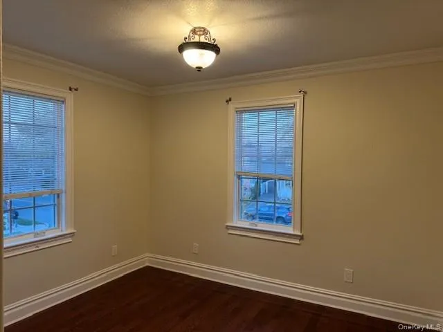 Empty room with ornamental molding, dark wood-type flooring, and a textured ceiling Empty room with ornamental molding, dark wood-type flooring, and a textured ceiling