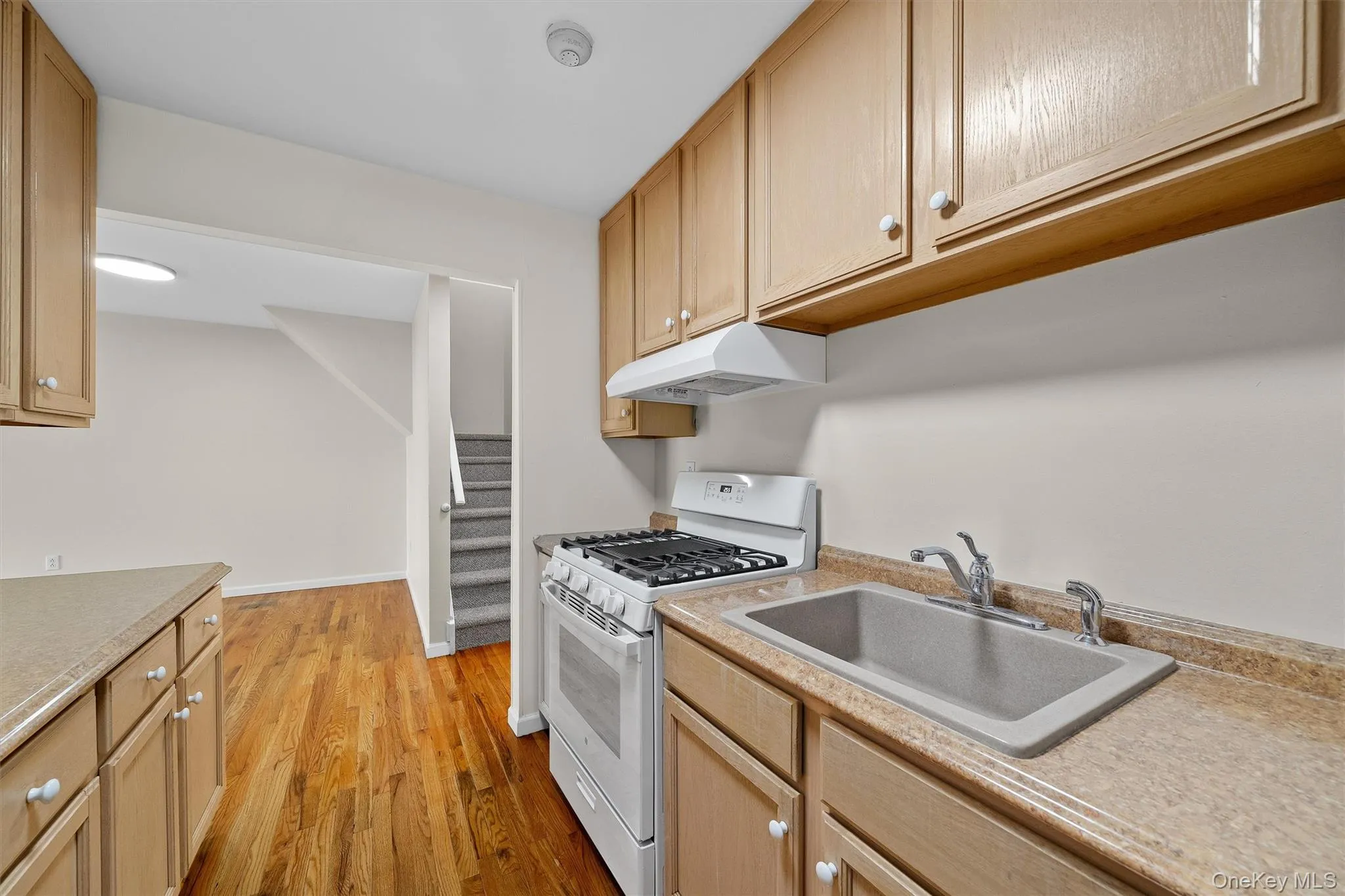 Kitchen featuring light wood-style flooring, under cabinet range hood, light countertops, white gas range, and a sink Kitchen featuring light wood-style flooring, under cabinet range hood, light countertops, white gas range, and a sink