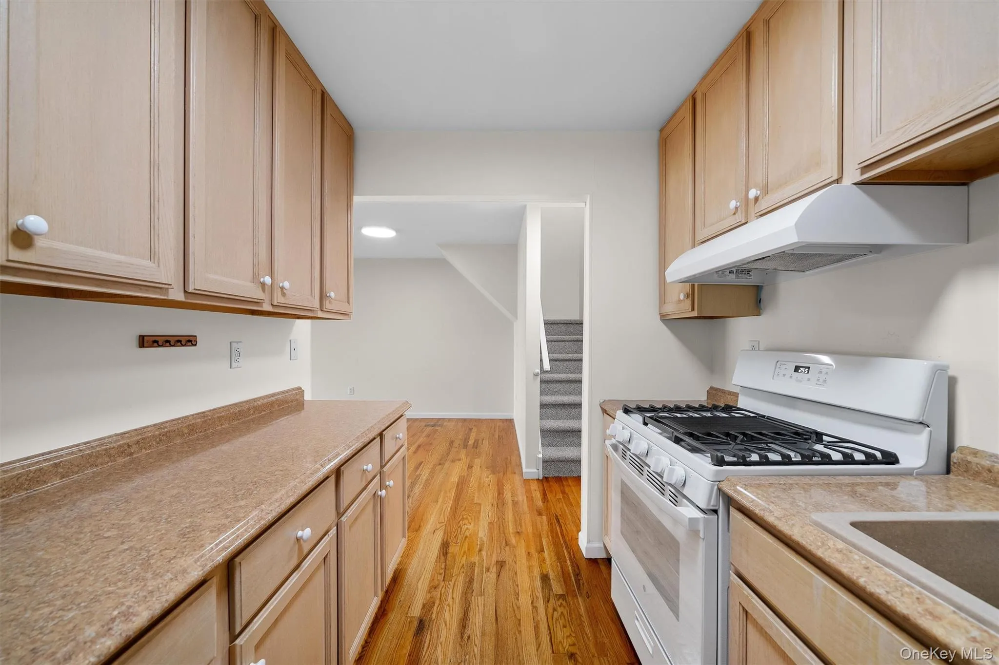 Kitchen with light brown cabinets, light wood-style floors, under cabinet range hood, light countertops, and white range with gas stovetop Kitchen with light brown cabinets, light wood-style floors, under cabinet range hood, light countertops, and white range with gas stovetop