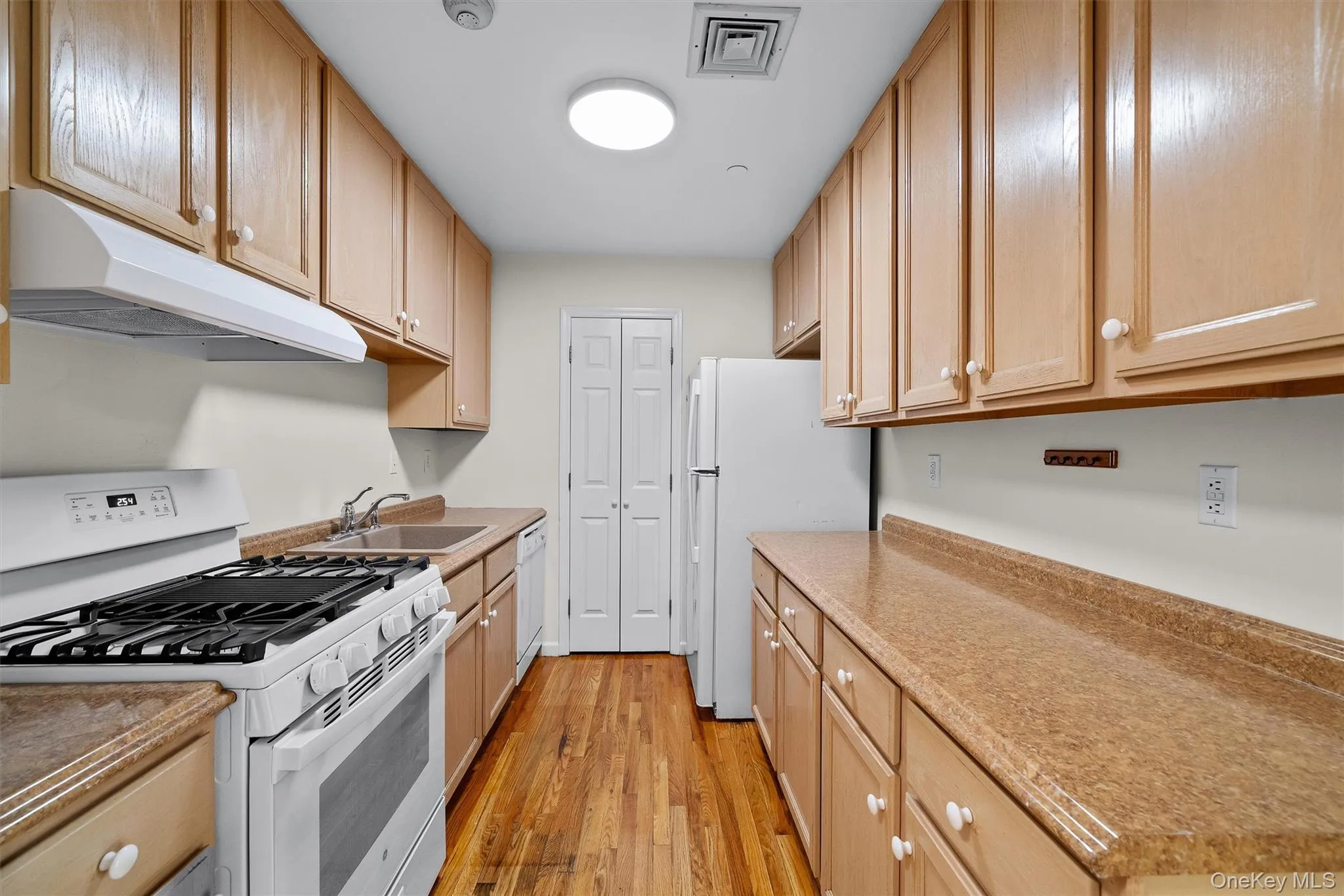 Kitchen with a sink, visible vents, under cabinet range hood, light wood-type flooring, and white appliances Kitchen with a sink, visible vents, under cabinet range hood, light wood-type flooring, and white appliances