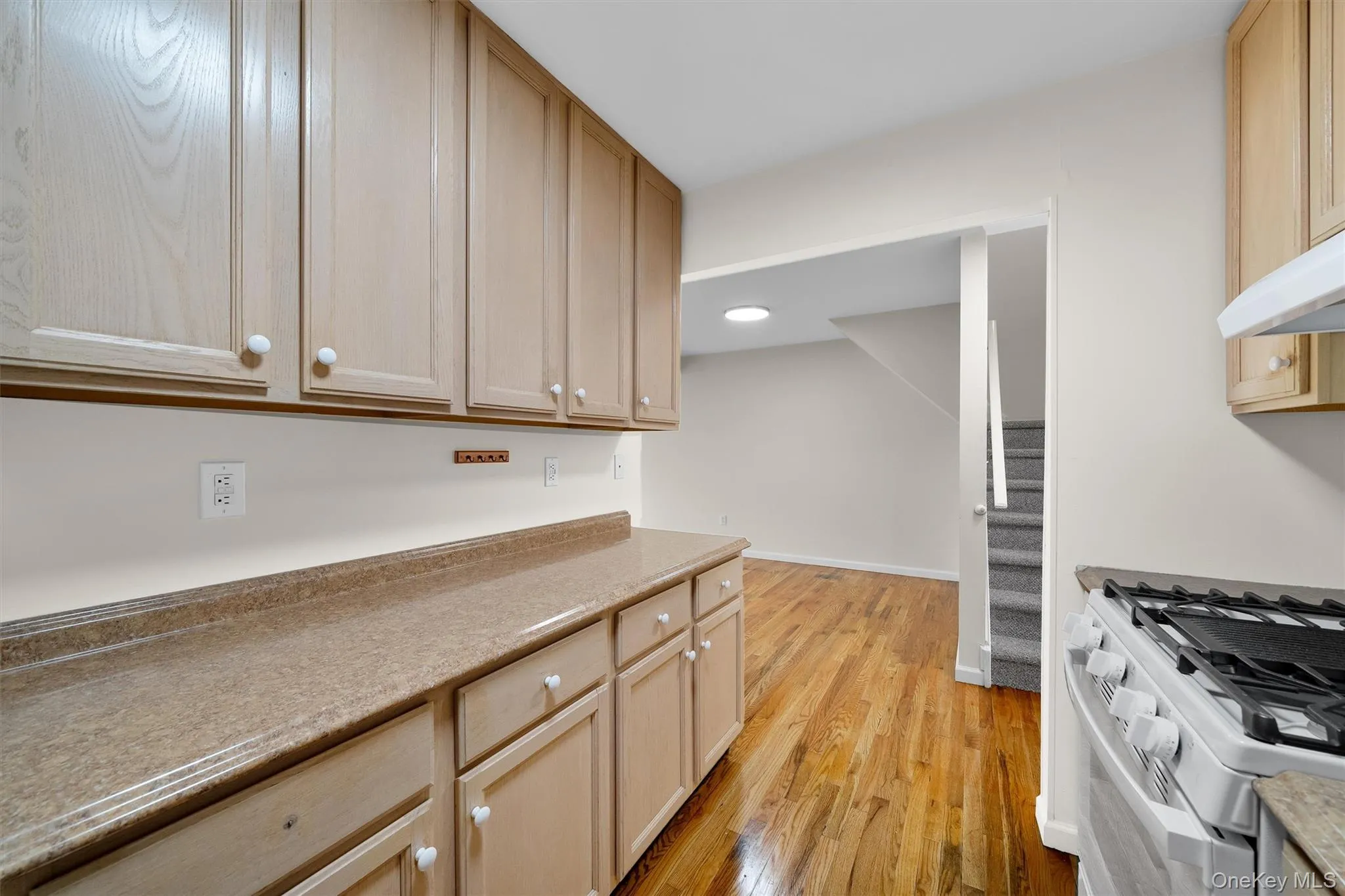 Kitchen with white range with gas stovetop, light wood-style flooring, and light brown cabinetry Kitchen with white range with gas stovetop, light wood-style flooring, and light brown cabinetry