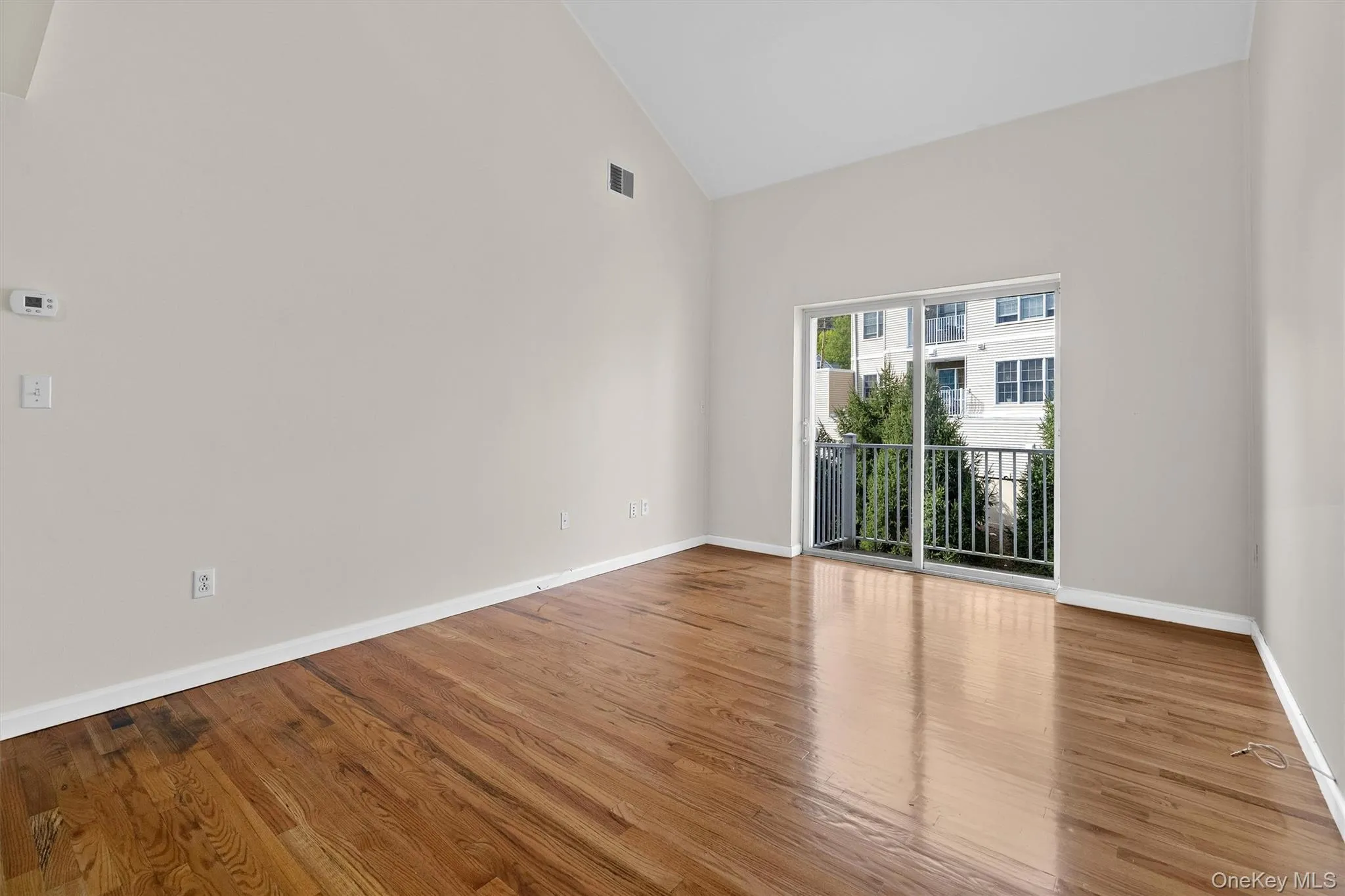 Empty room featuring visible vents, wood finished floors, and high vaulted ceiling Empty room featuring visible vents, wood finished floors, and high vaulted ceiling