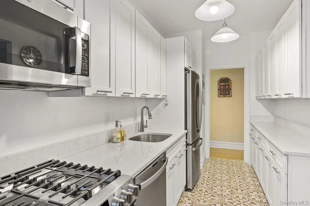 Kitchen with stainless steel appliances, light stone counters, white cabinetry, and hanging light fixtures Kitchen with stainless steel appliances, light stone counters, white cabinetry, and hanging light fixtures