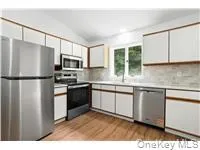 Kitchen featuring appliances with stainless steel finishes, light countertops, white cabinetry, light wood-type flooring, and vaulted ceiling Kitchen featuring appliances with stainless steel finishes, light countertops, white cabinetry, light wood-type flooring, and vaulted ceiling