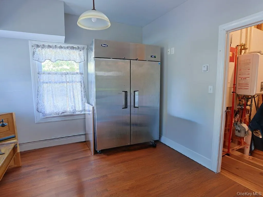 Kitchen featuring dark wood finished floors, high end fridge, a baseboard heating unit, decorative light fixtures, and tankless water heater Kitchen featuring dark wood finished floors, high end fridge, a baseboard heating unit, decorative light fixtures, and tankless water heater