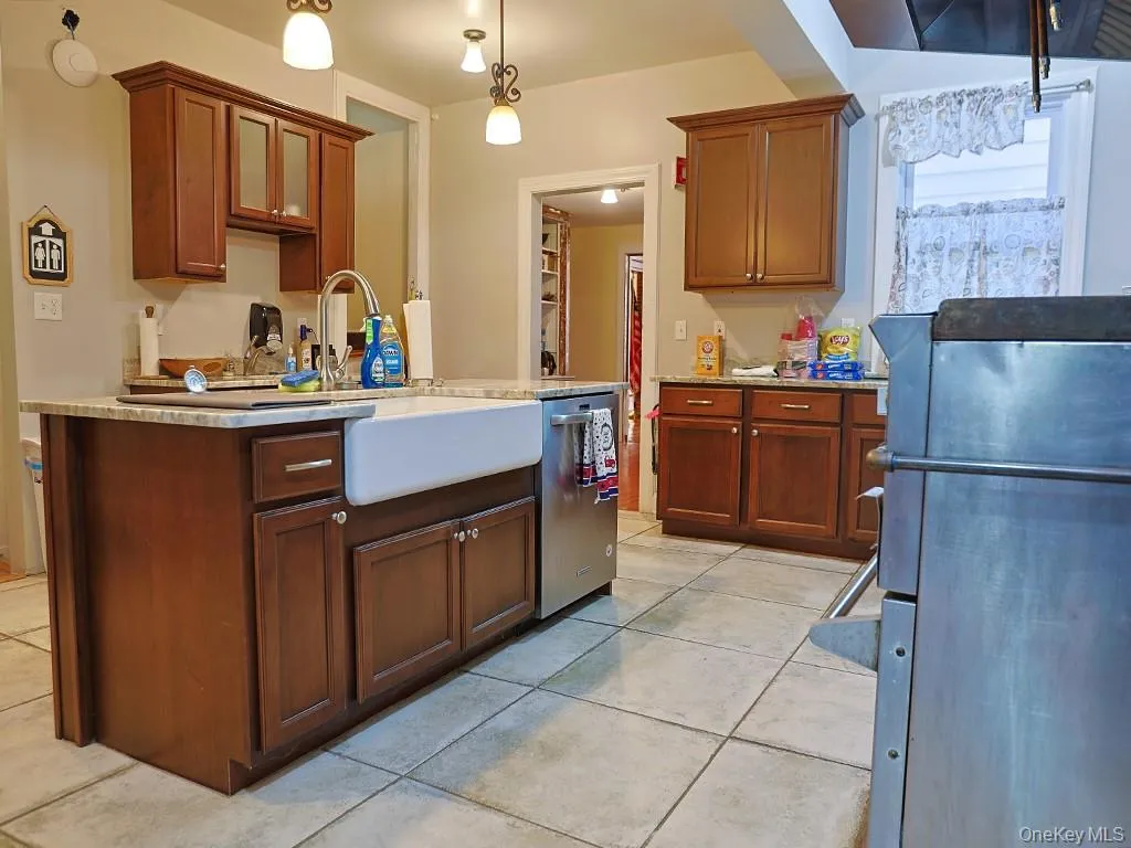 Kitchen with hanging light fixtures, light tile patterned flooring, stainless steel appliances, light stone countertops, and a center island with sink Kitchen with hanging light fixtures, light tile patterned flooring, stainless steel appliances, light stone countertops, and a center island with sink