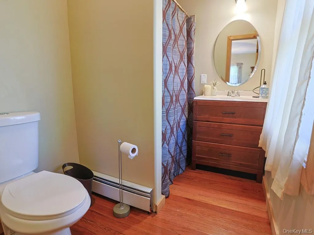 Full bathroom with baseboard heating, vanity, a shower with shower curtain, and light wood-style floors Full bathroom with baseboard heating, vanity, a shower with shower curtain, and light wood-style floors