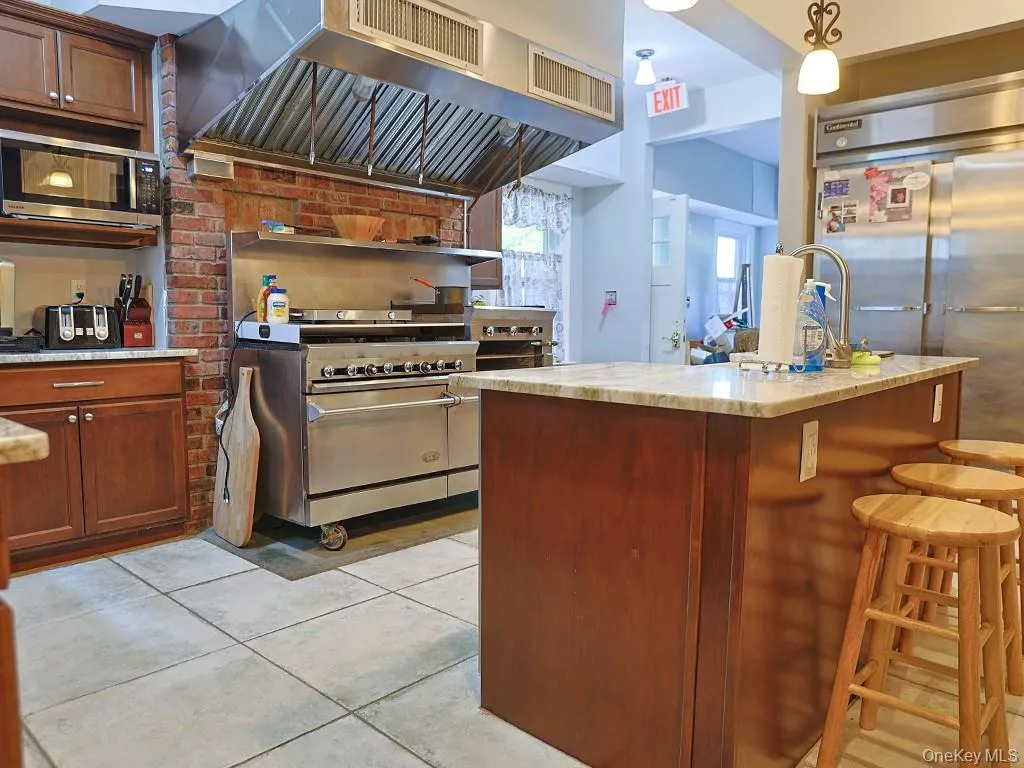Kitchen featuring custom exhaust hood, stainless steel appliances, hanging light fixtures, light stone countertops, and a breakfast bar Kitchen featuring custom exhaust hood, stainless steel appliances, hanging light fixtures, light stone countertops, and a breakfast bar