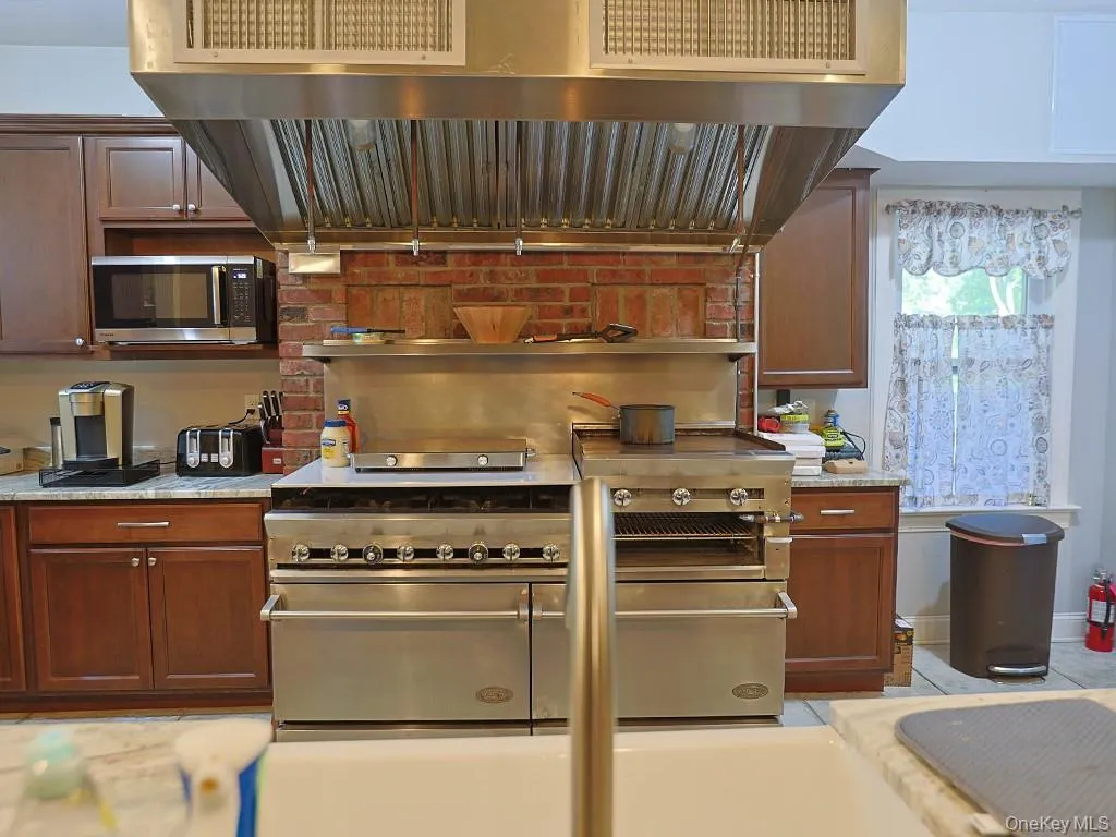 Kitchen featuring ventilation hood, stainless steel appliances, and light stone countertops Kitchen featuring ventilation hood, stainless steel appliances, and light stone countertops