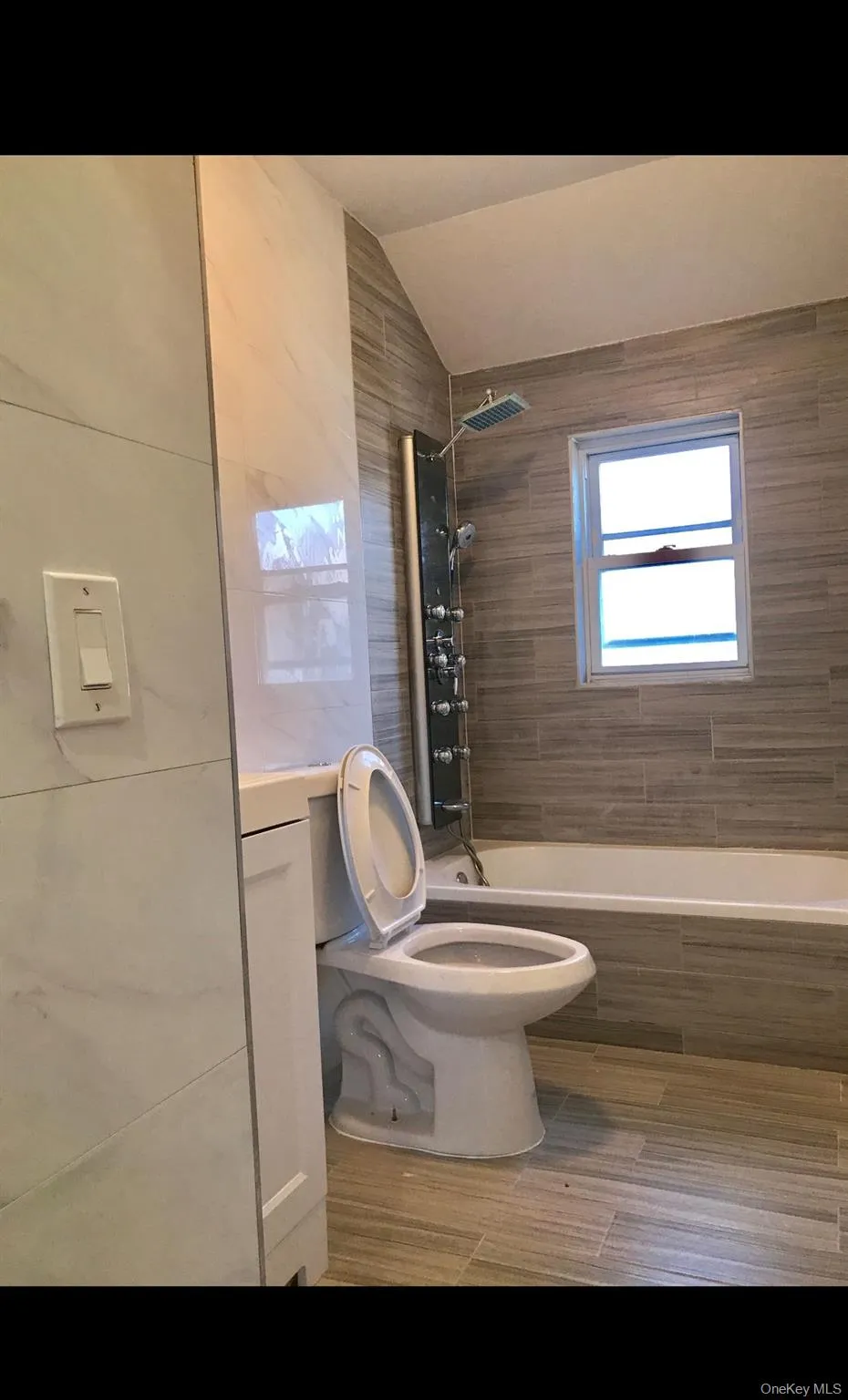 Full bath with tile walls, vaulted ceiling, tiled shower / bath, and wood tiled floors Full bath with tile walls, vaulted ceiling, tiled shower / bath, and wood tiled floors