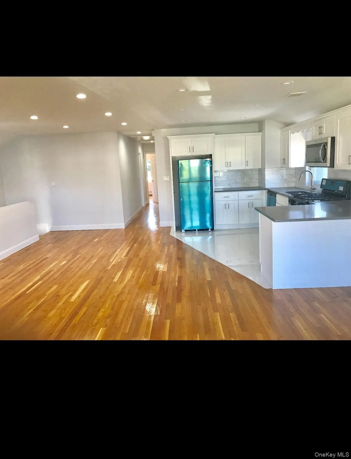 Kitchen featuring freestanding refrigerator, white cabinetry, stainless steel microwave, black range with gas cooktop, and decorative backsplash Kitchen featuring freestanding refrigerator, white cabinetry, stainless steel microwave, black range with gas cooktop, and decorative backsplash