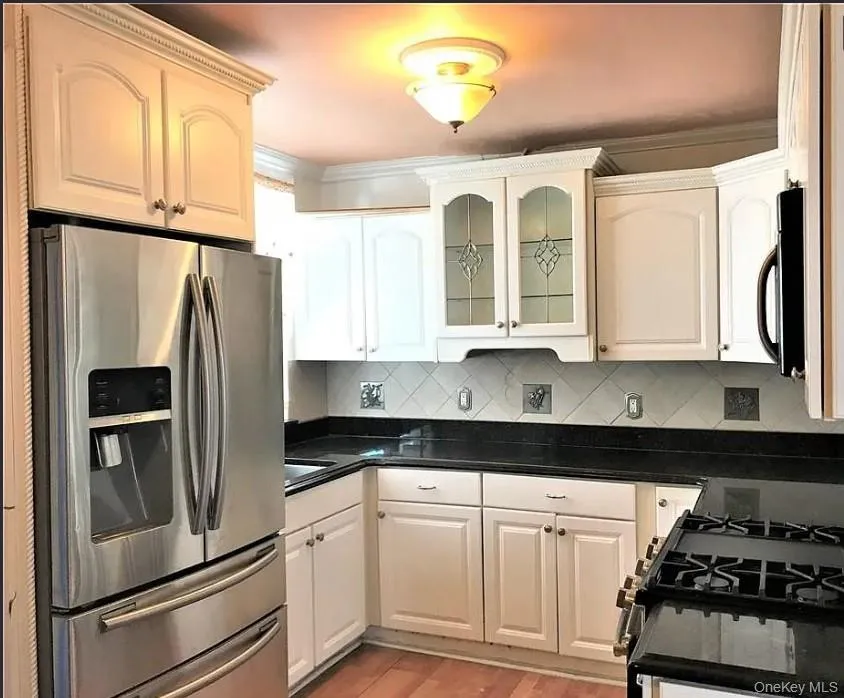Kitchen featuring stainless steel fridge with ice dispenser, backsplash, range with gas cooktop, glass insert cabinets, and black microwave Kitchen featuring stainless steel fridge with ice dispenser, backsplash, range with gas cooktop, glass insert cabinets, and black microwave