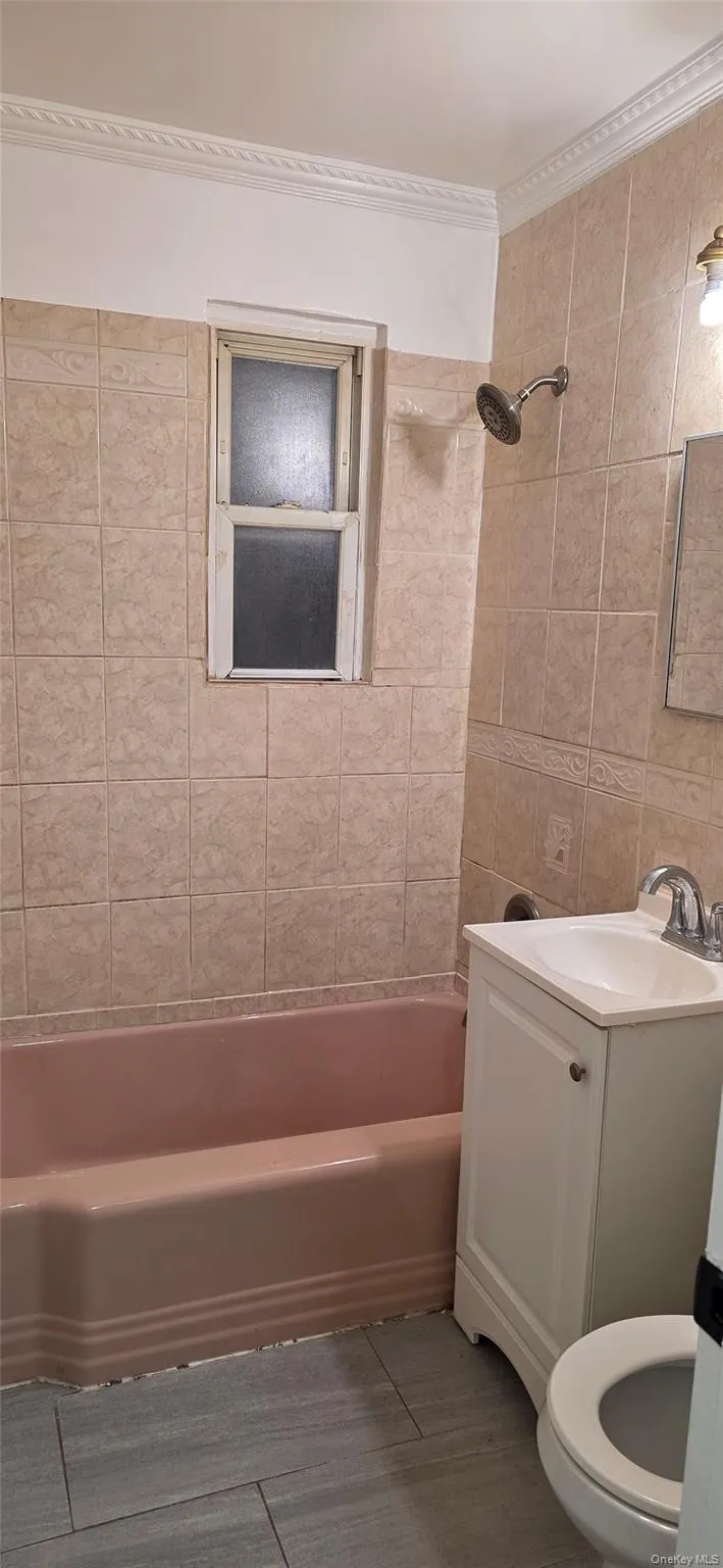 Bathroom with shower / tub combination, vanity, ornamental molding, light tile patterned floors, and tile walls Bathroom with shower / tub combination, vanity, ornamental molding, light tile patterned floors, and tile walls