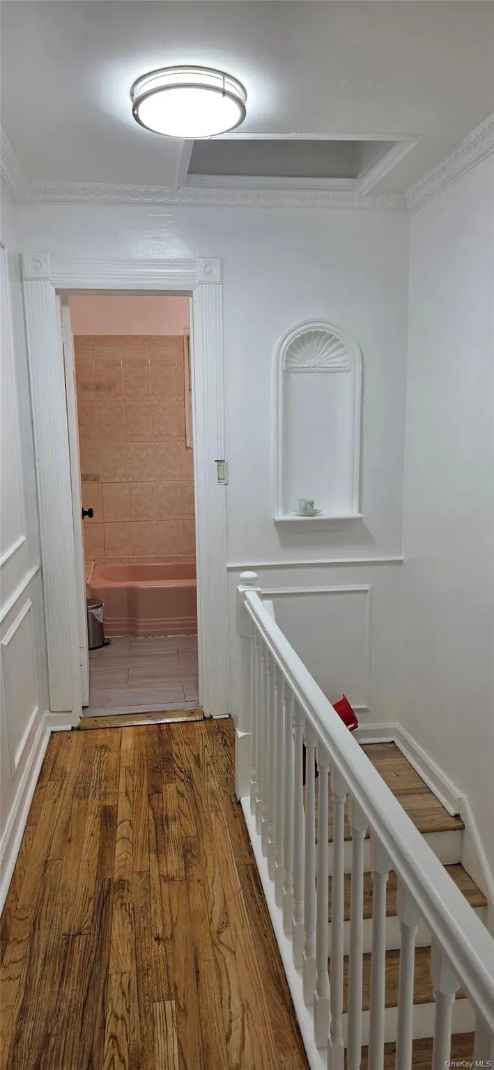 Hallway with light wood-style flooring, ornamental molding, and an upstairs landing Hallway with light wood-style flooring, ornamental molding, and an upstairs landing
