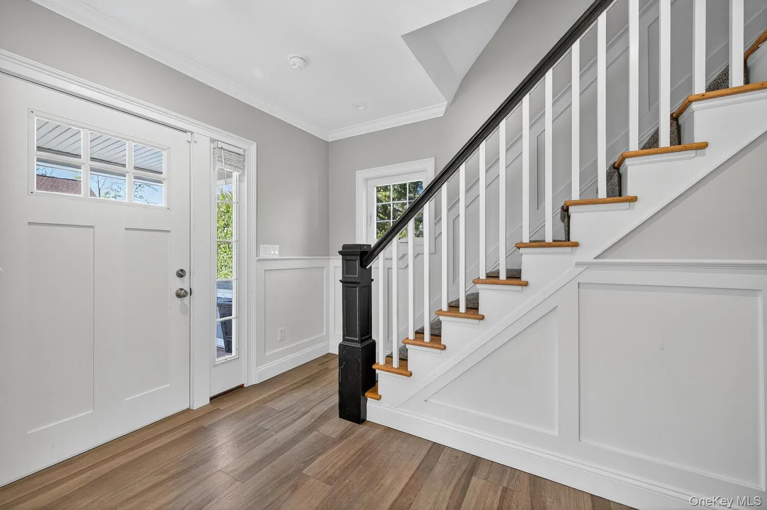 Foyer featuring wood finished floors, crown molding, a decorative wall, stairway, and a wainscoted wall Foyer featuring wood finished floors, crown molding, a decorative wall, stairway, and a wainscoted wall