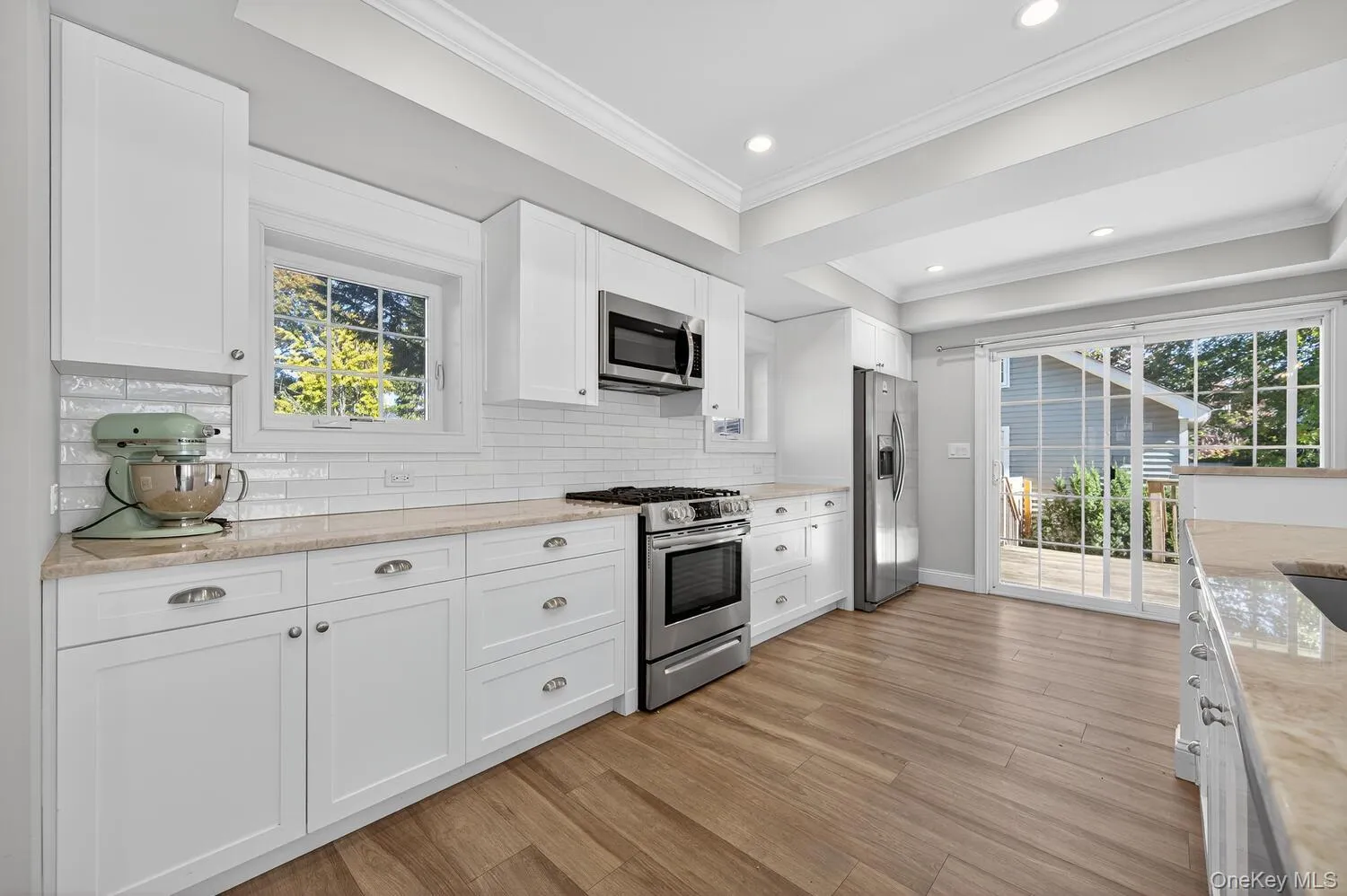 Kitchen with appliances with stainless steel finishes, decorative backsplash, white cabinets, healthy amount of natural light, and ornamental molding Kitchen with appliances with stainless steel finishes, decorative backsplash, white cabinets, healthy amount of natural light, and ornamental molding
