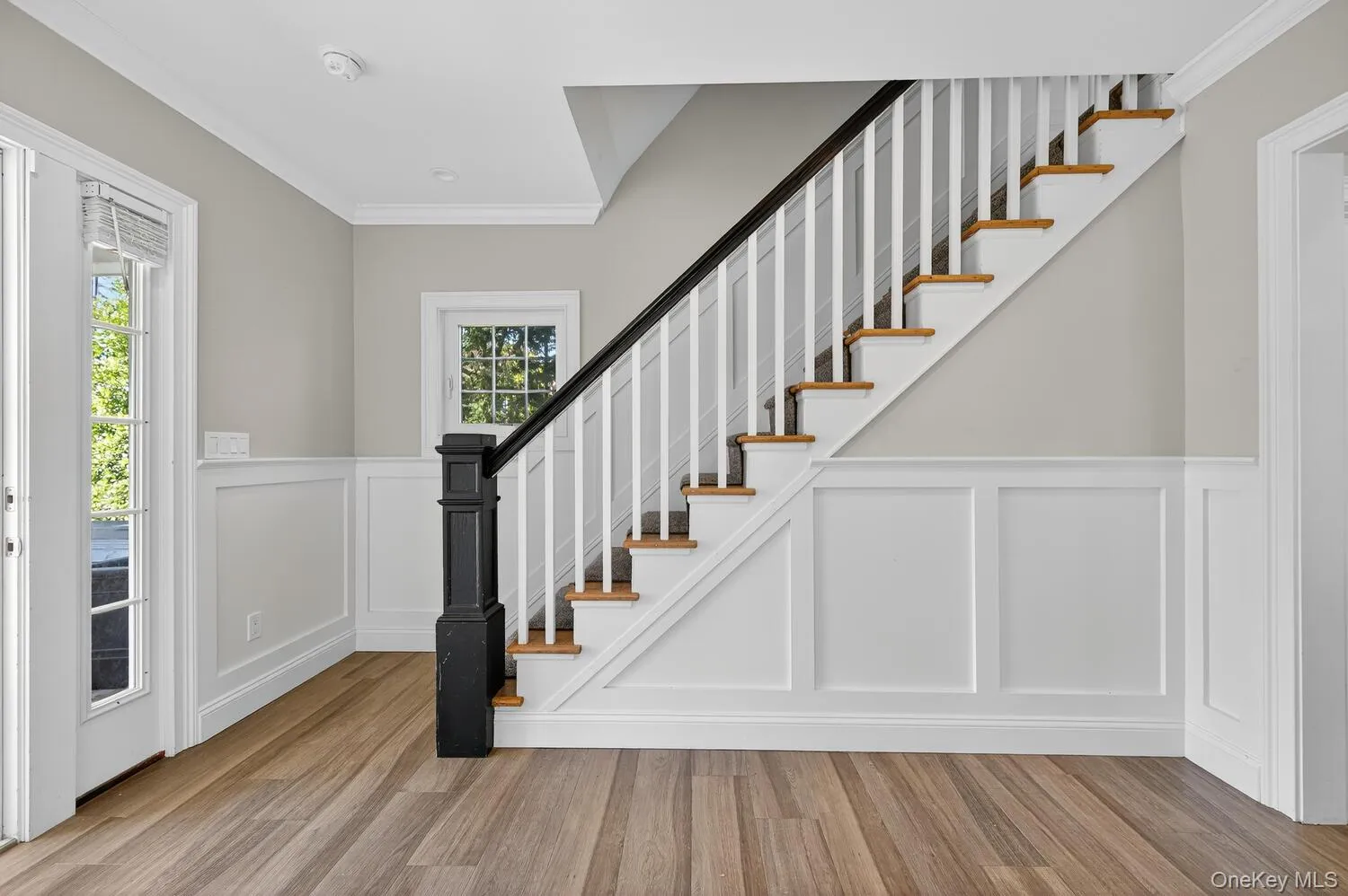 Entryway with crown molding, light wood-style floors, stairs, a decorative wall, and wainscoting Entryway with crown molding, light wood-style floors, stairs, a decorative wall, and wainscoting