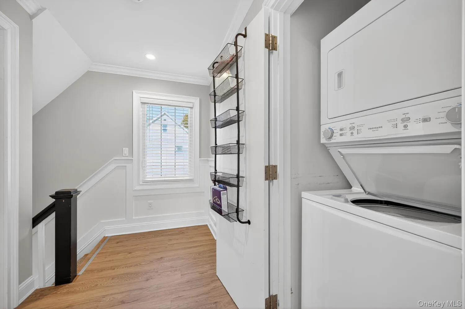 Laundry room featuring light wood finished floors, estacked washer and dryer, a wainscoted wall, a decorative wall, and ornamental molding Laundry room featuring light wood finished floors, estacked washer and dryer, a wainscoted wall, a decorative wall, and ornamental molding