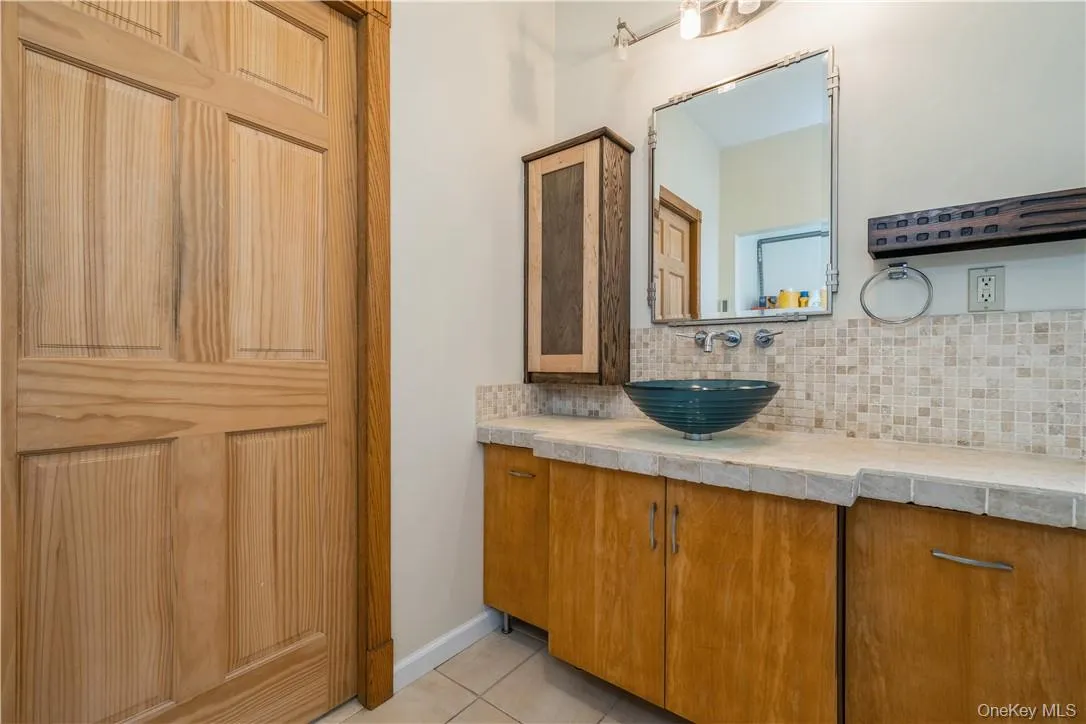 Large bathroom near front door features stylish tile and glass bowl sink. Large bathroom near front door features stylish tile and glass bowl sink.