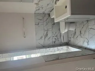 Full bathroom with vanity, tile walls, wainscoting, light marble finish floors, and baseboard heating Full bathroom with vanity, tile walls, wainscoting, light marble finish floors, and baseboard heating